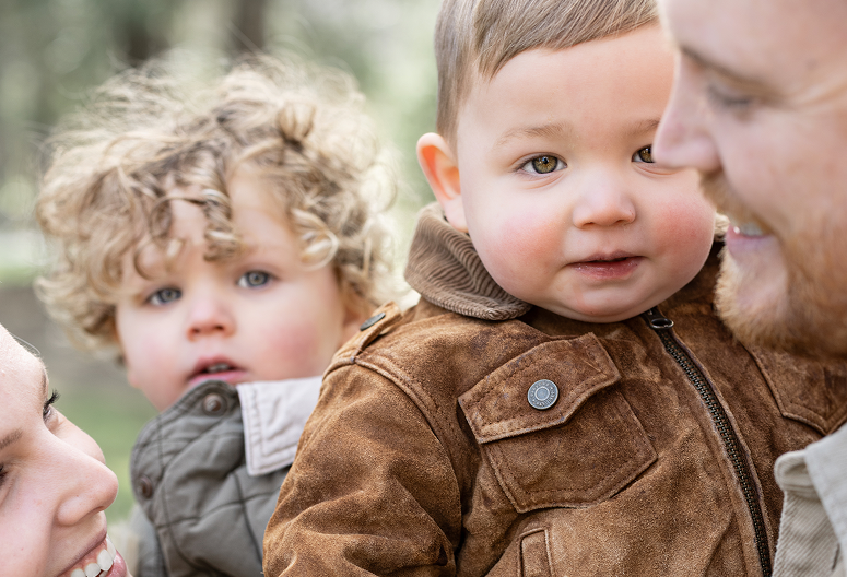 Close-up of a father with two young children outdoors, smiling and looking at each other.