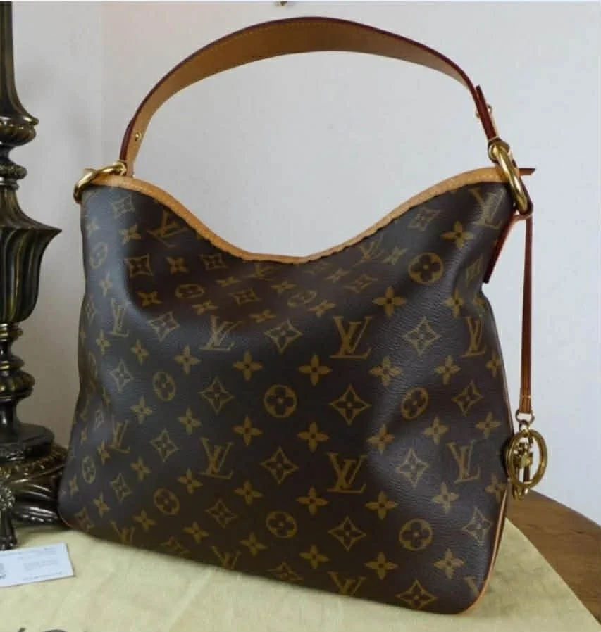 A Louis Vuitton monogram canvas handbag with leather trim, placed on a yellow cloth surface.