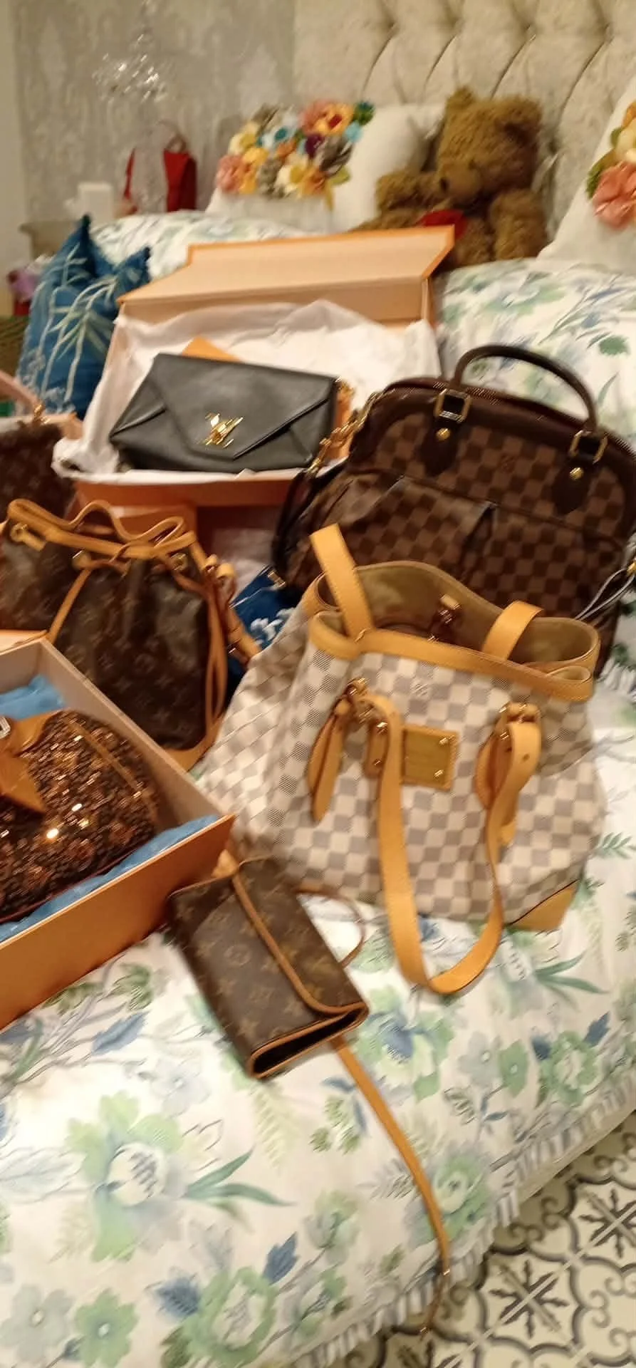 Various handbags and accessories placed on a floral bedspread in a bedroom.