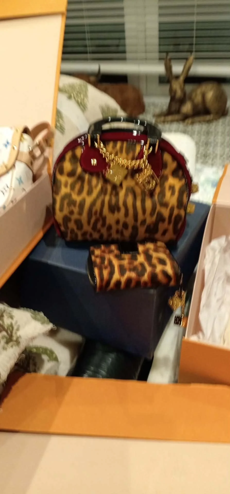 A leopard print handbag with gold chain and charm, placed on top of a dark blue box, with a smaller matching leopard print pouch attached to the bag.