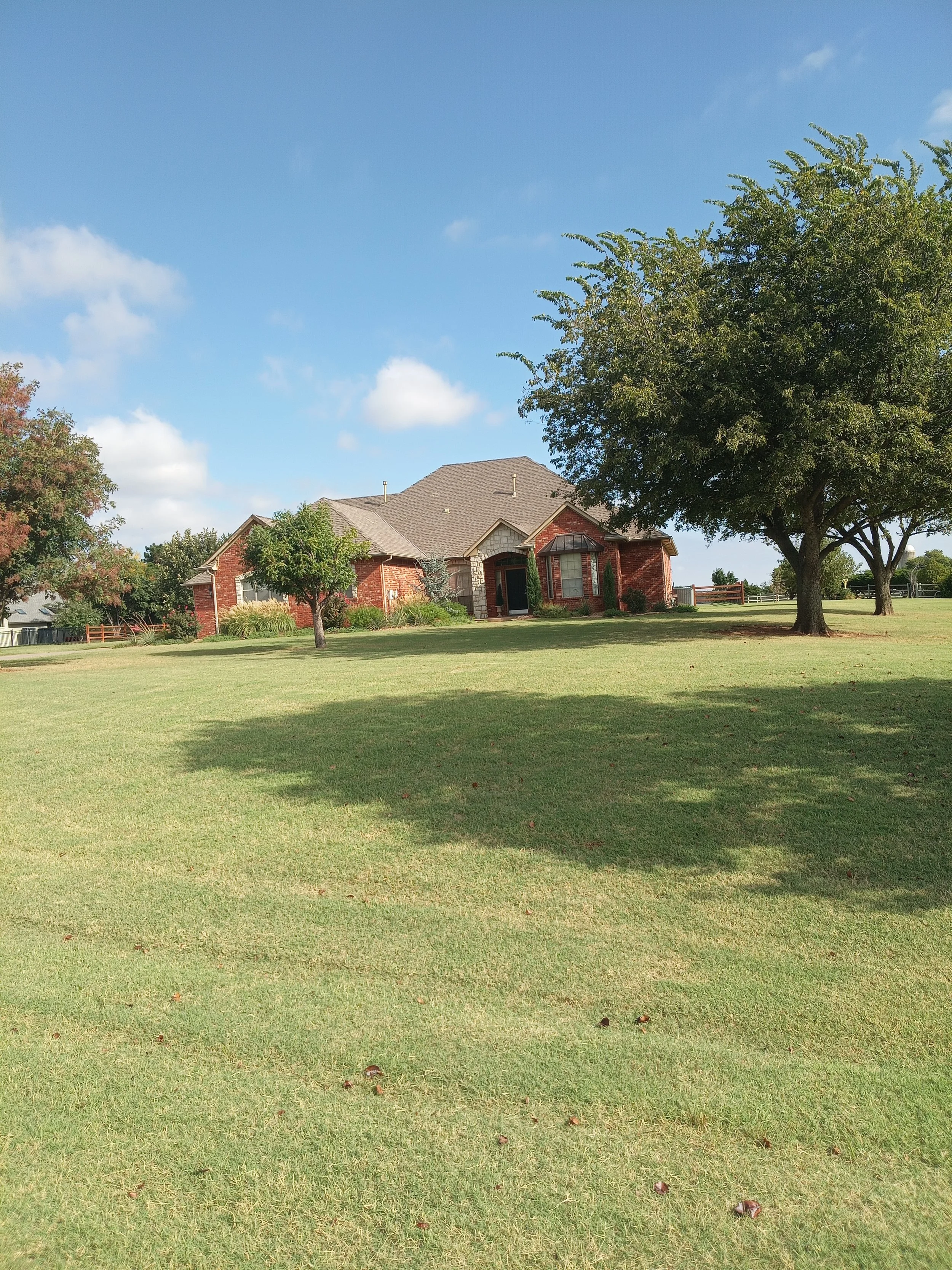 A spacious lawn in front of a brick house with a new gabled roof, surrounded by trees, under a partly cloudy sky.