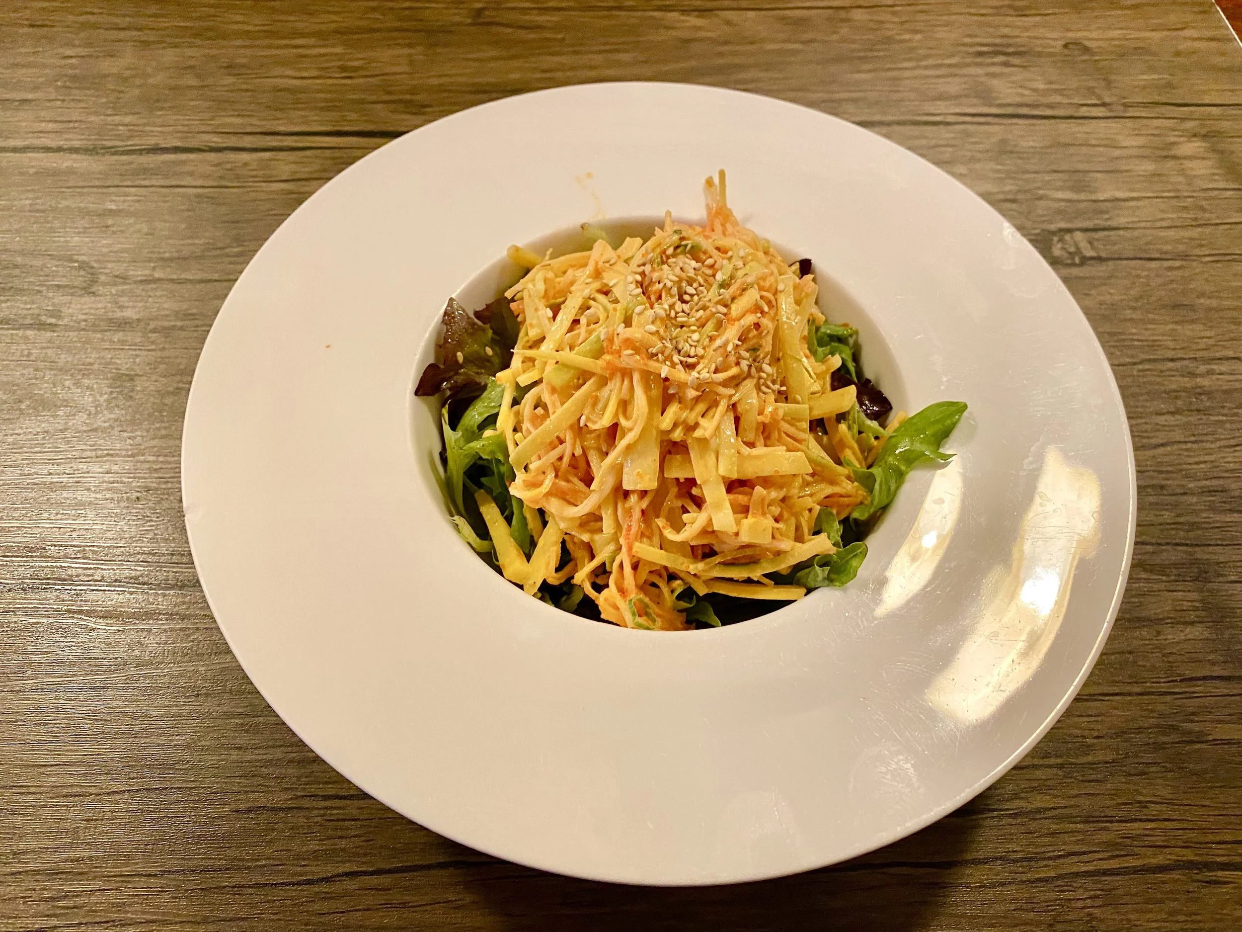 A plate of Asian-style noodle salad topped with sesame seeds on a wooden table.