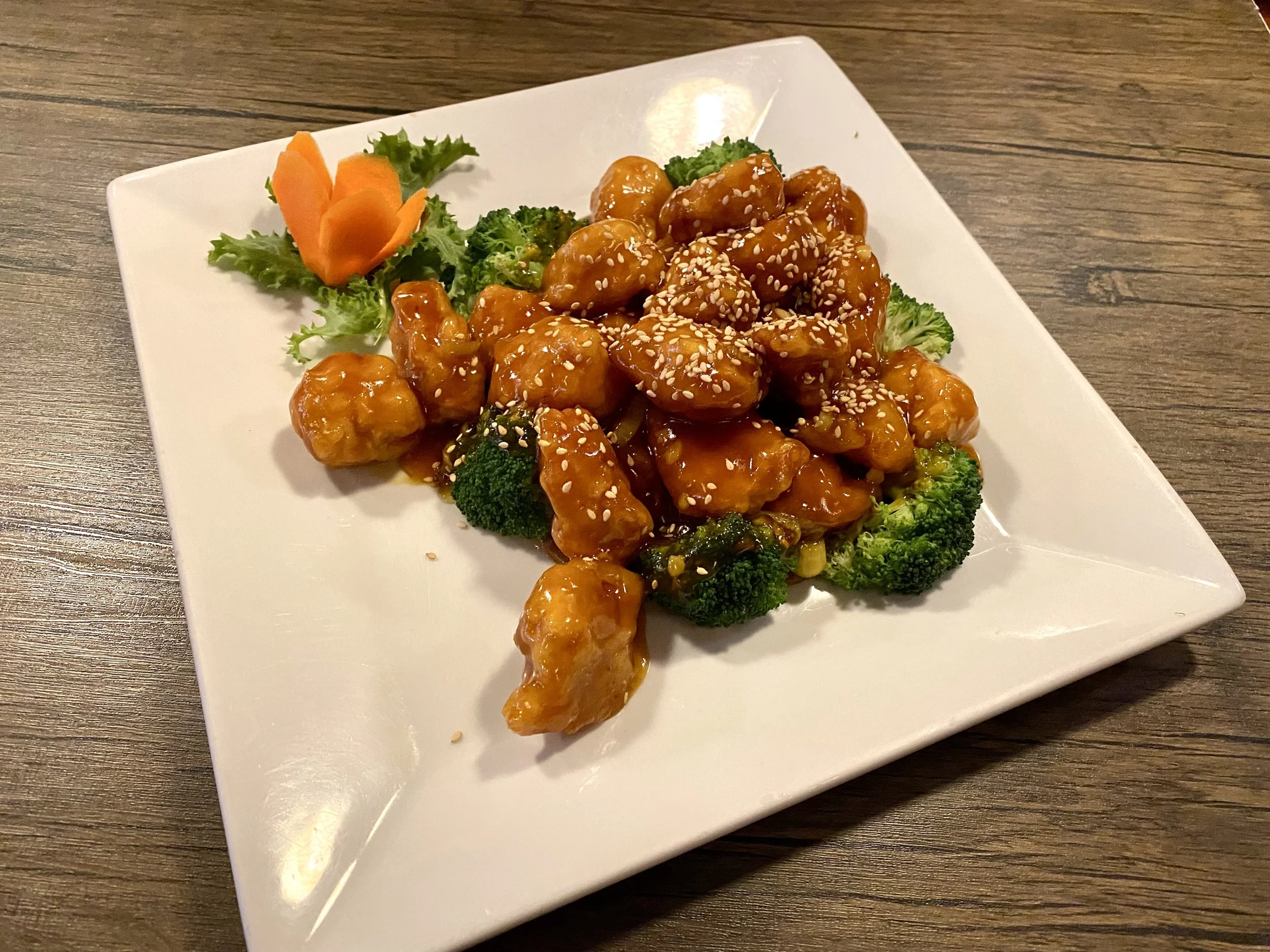 Sweet and sour chicken with vegetables on a white square plate.