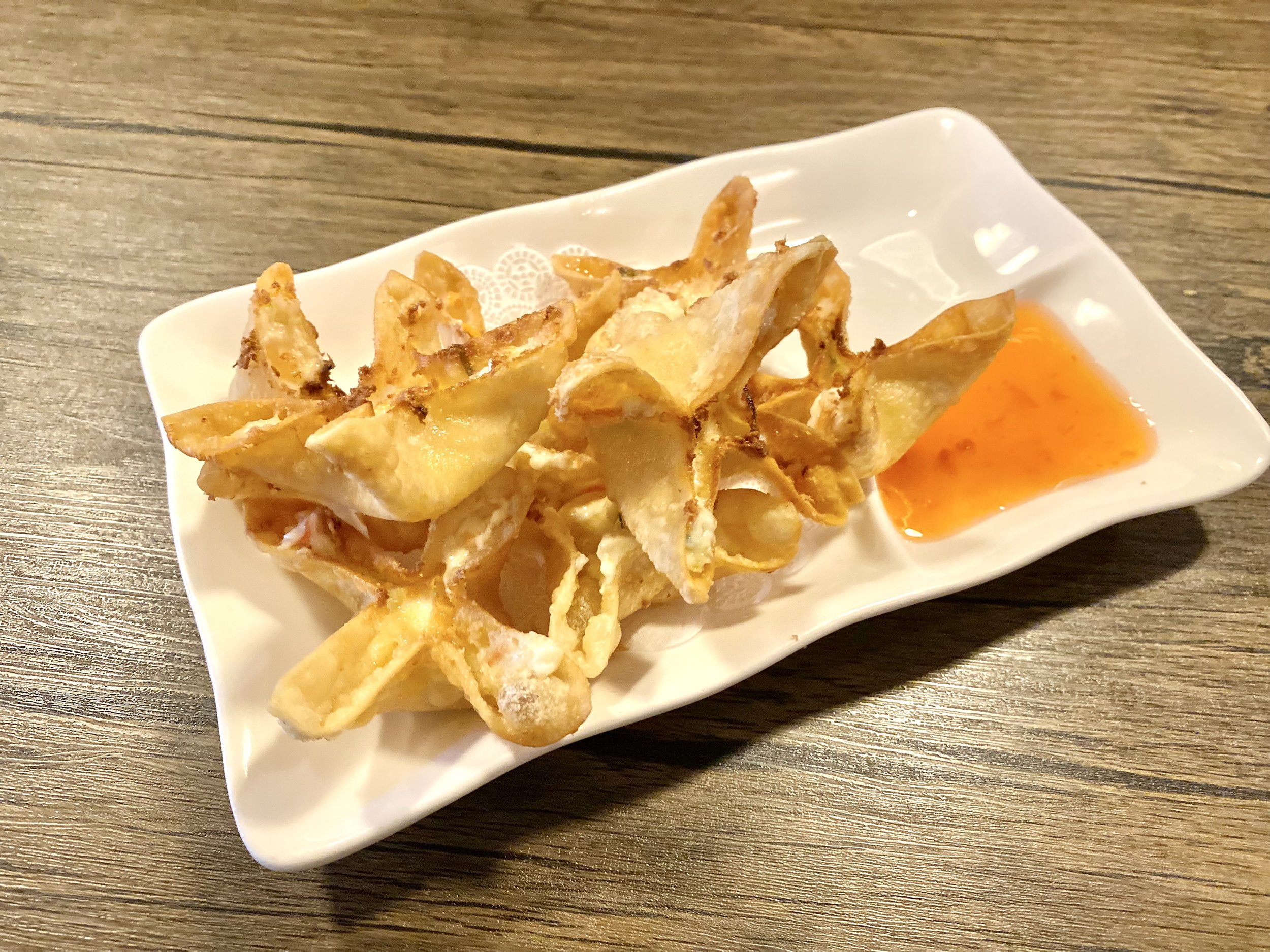 Fried wontons served on a white dish with a side of orange dipping sauce.