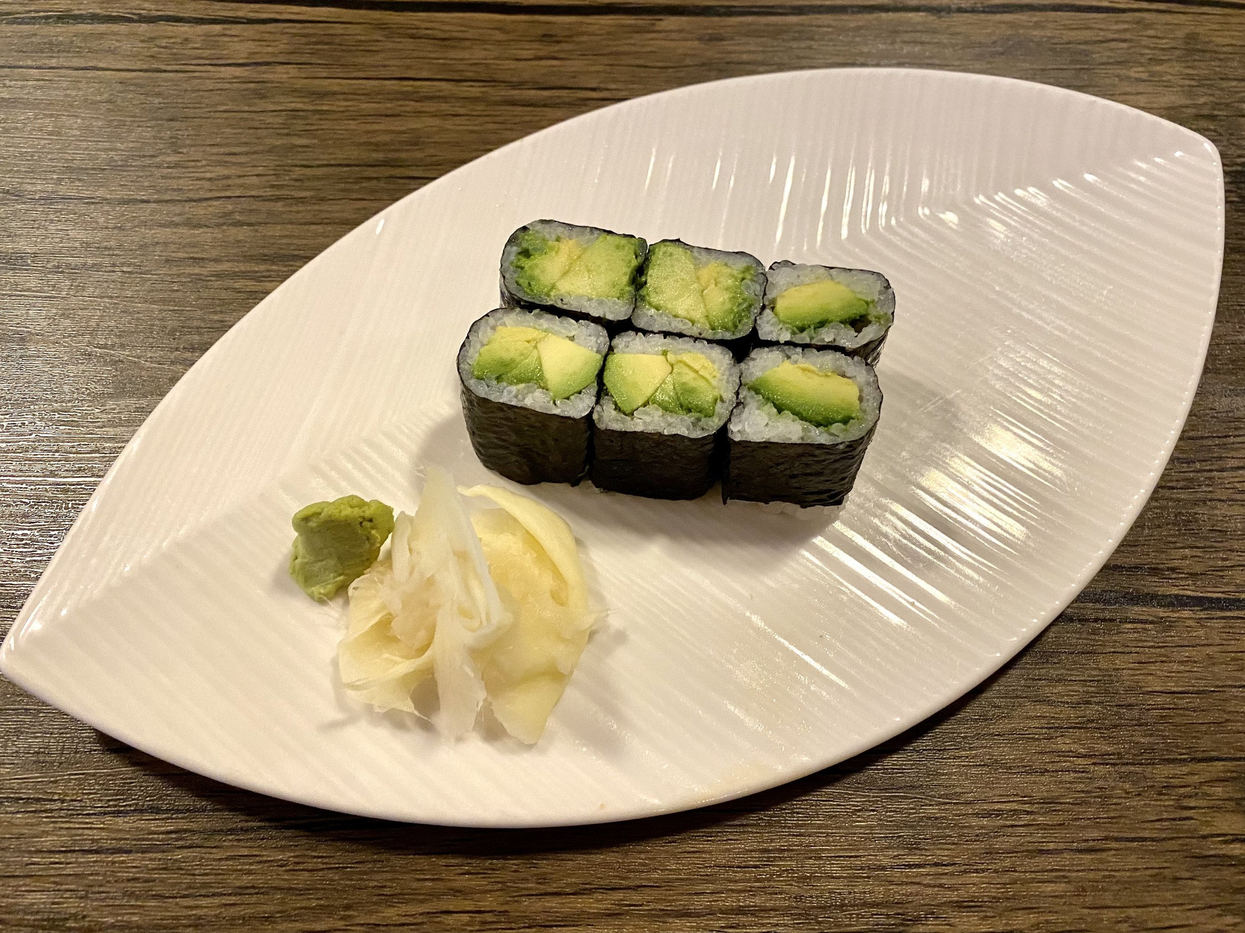 Six pieces of avocado sushi rolls with wasabi and pickled ginger on a white plate.