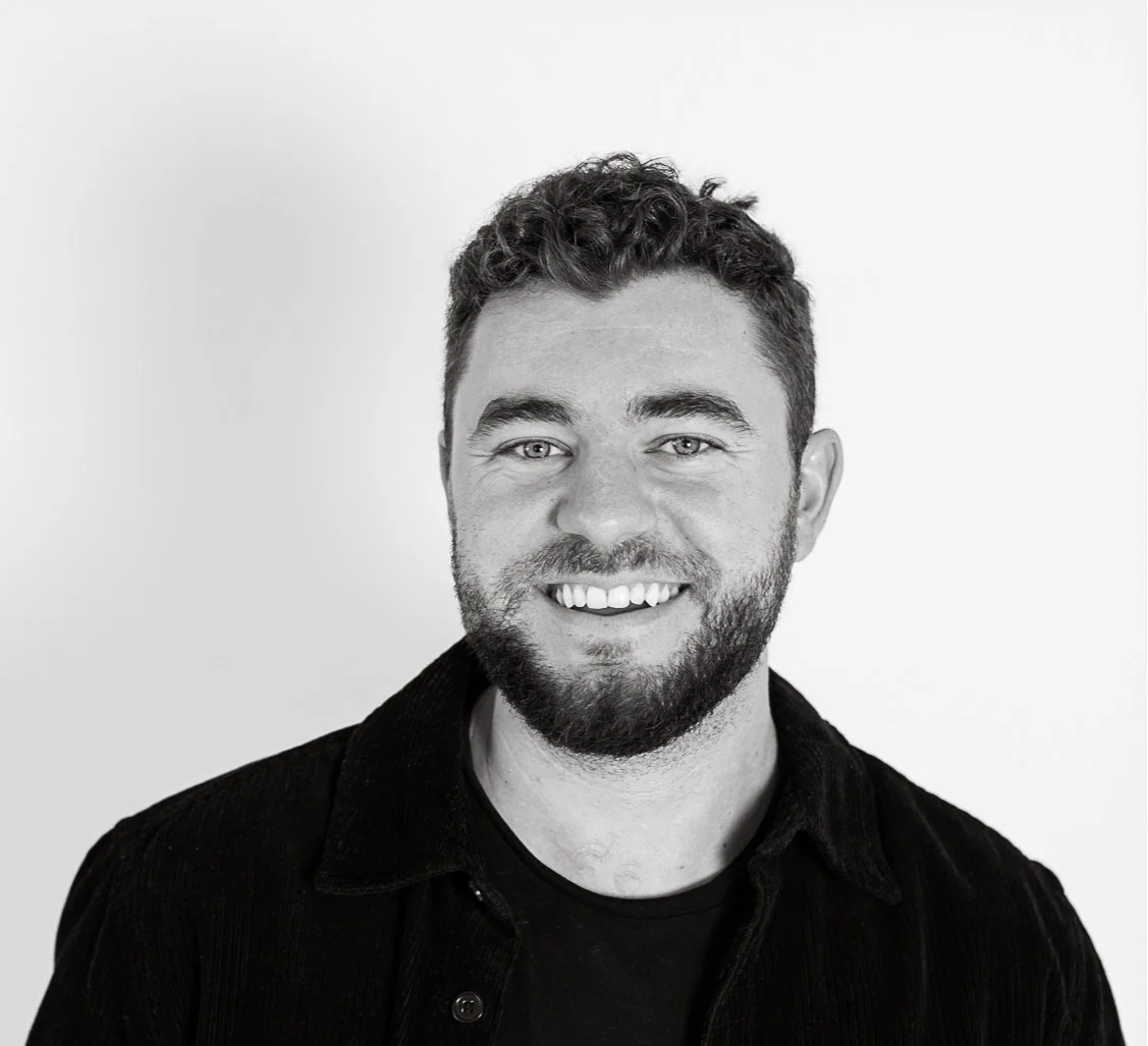 Black and white portrait of a smiling man with curly hair and a beard, wearing a dark shirt, against a plain background.