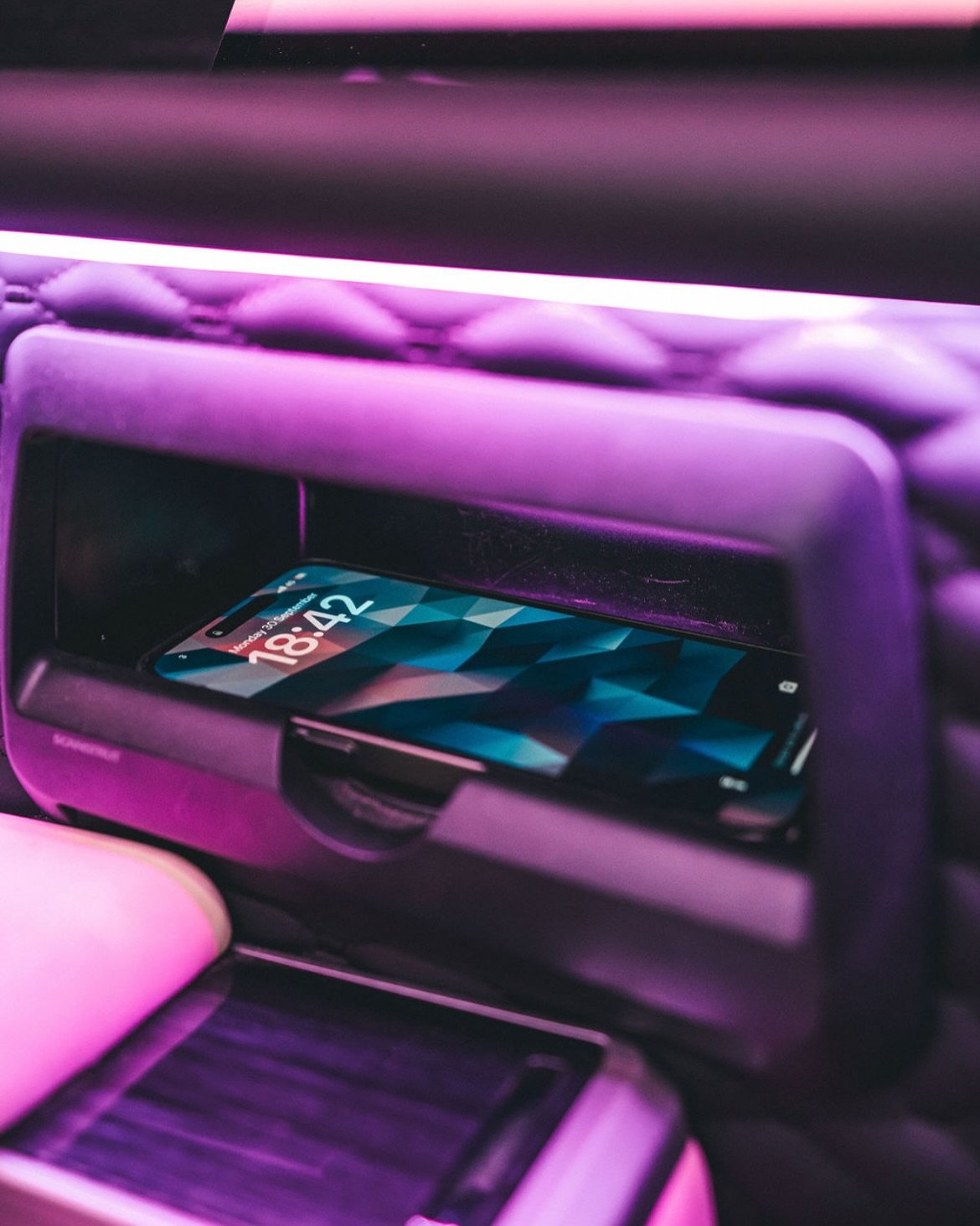 A smartphone with a digital display resting in a slot inside a vehicle's dashboard or entertainment system.