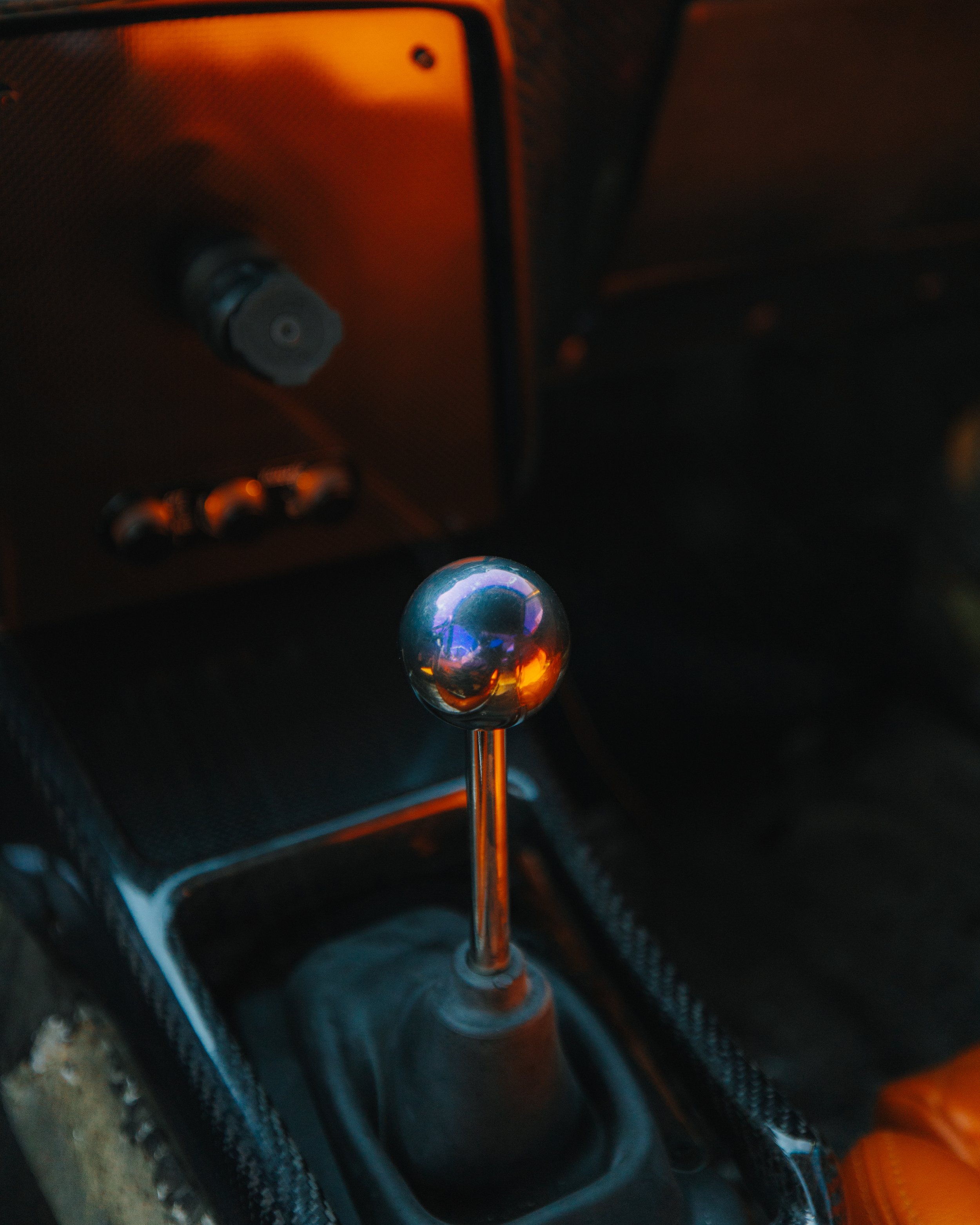 Close-up of a silver gear shift knob in a car interior, with a black textured console and dashboard in the background.
