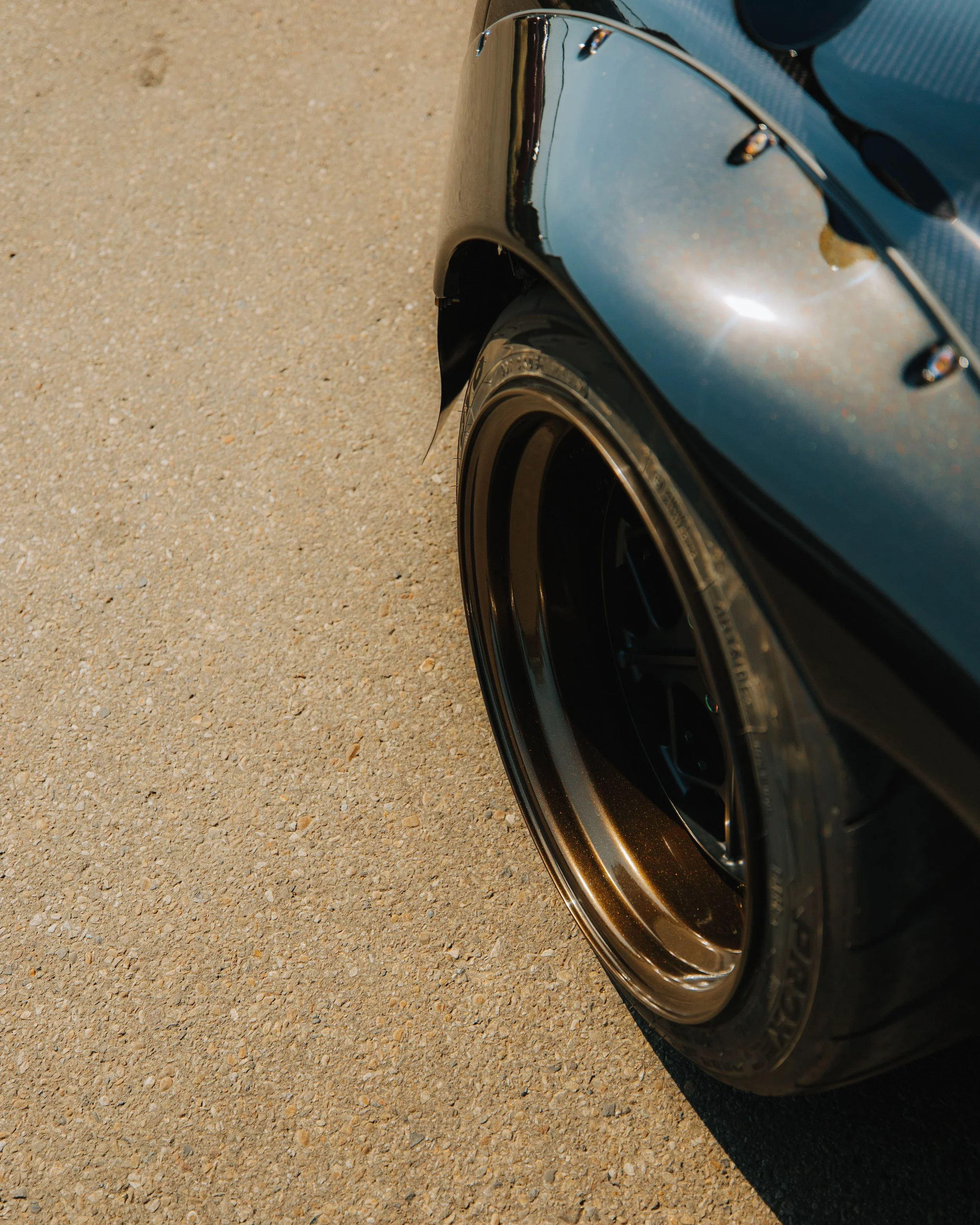 Close-up of a black car's front fender and tire on a sandy surface.