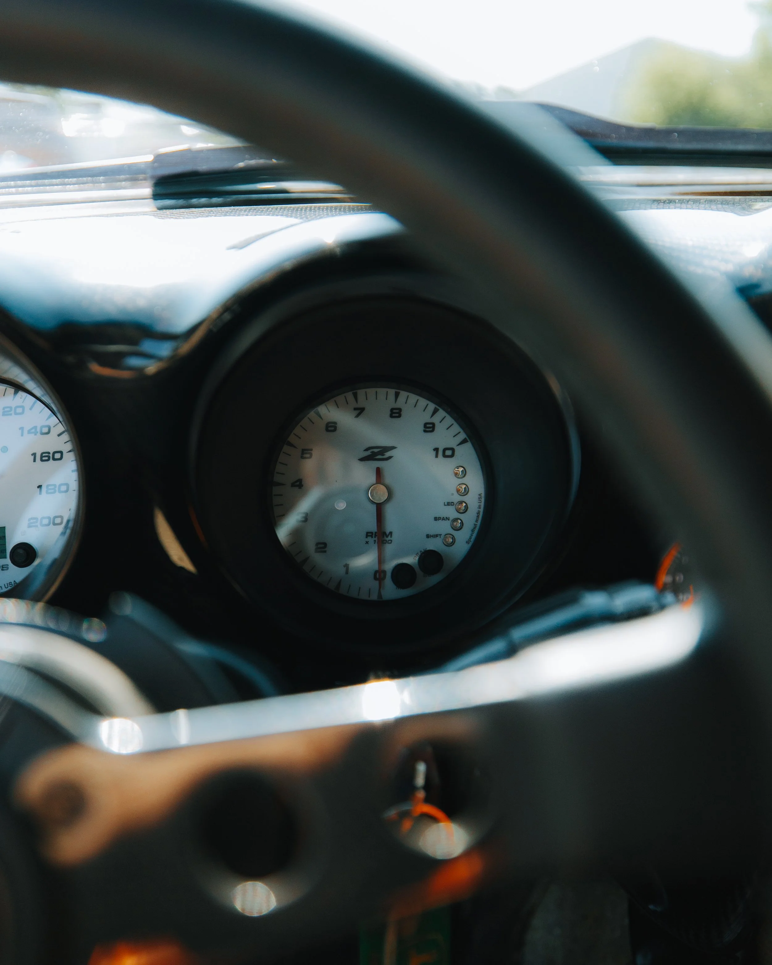 Close-up of a car dashboard with an analog tachometer showing around 1,000 RPM in sunlight.