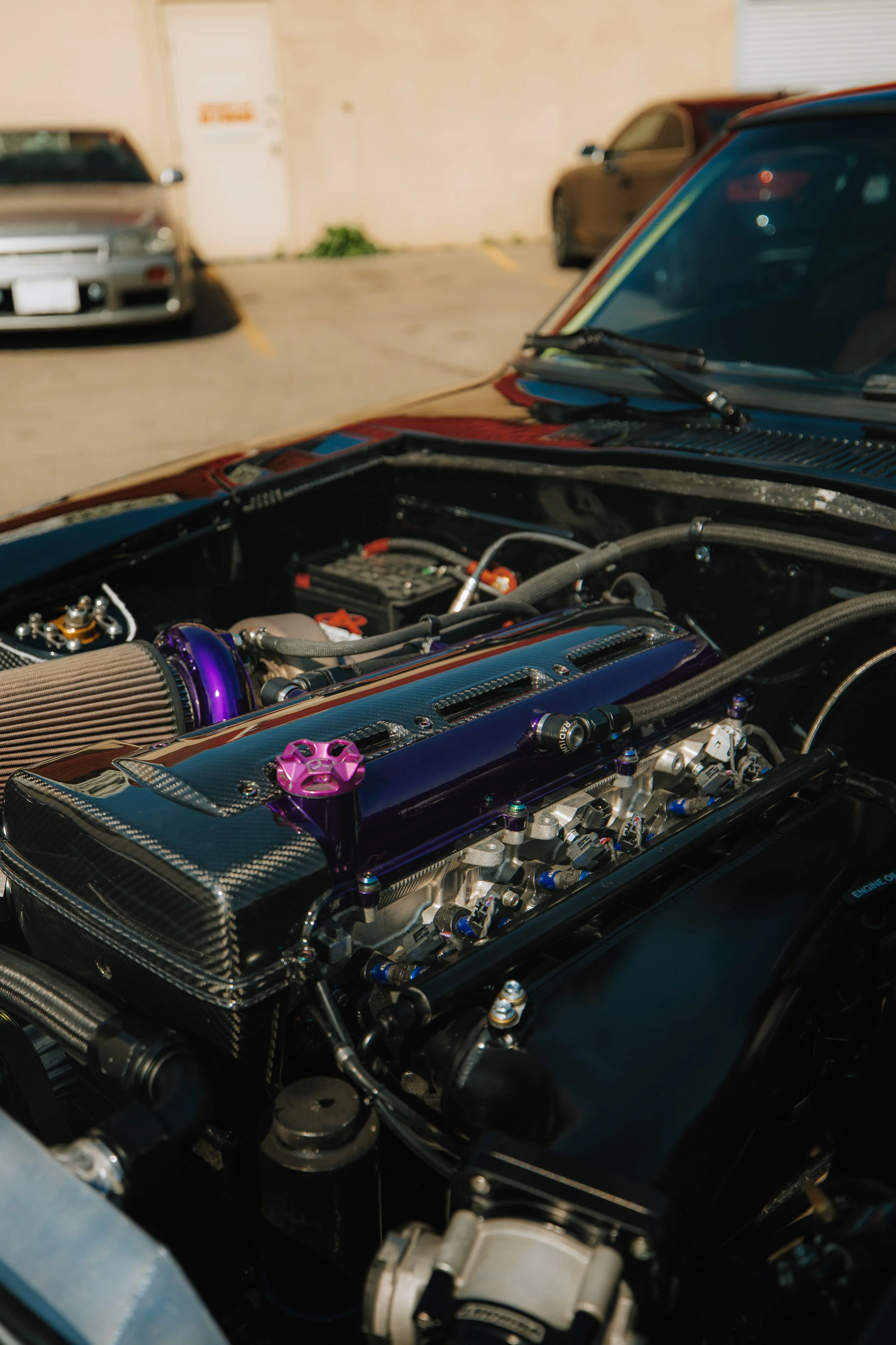 View of a high-performance car engine with aftermarket parts, including a purple intake manifold, carbon fiber components, and custom fittings, situated under an open hood.
