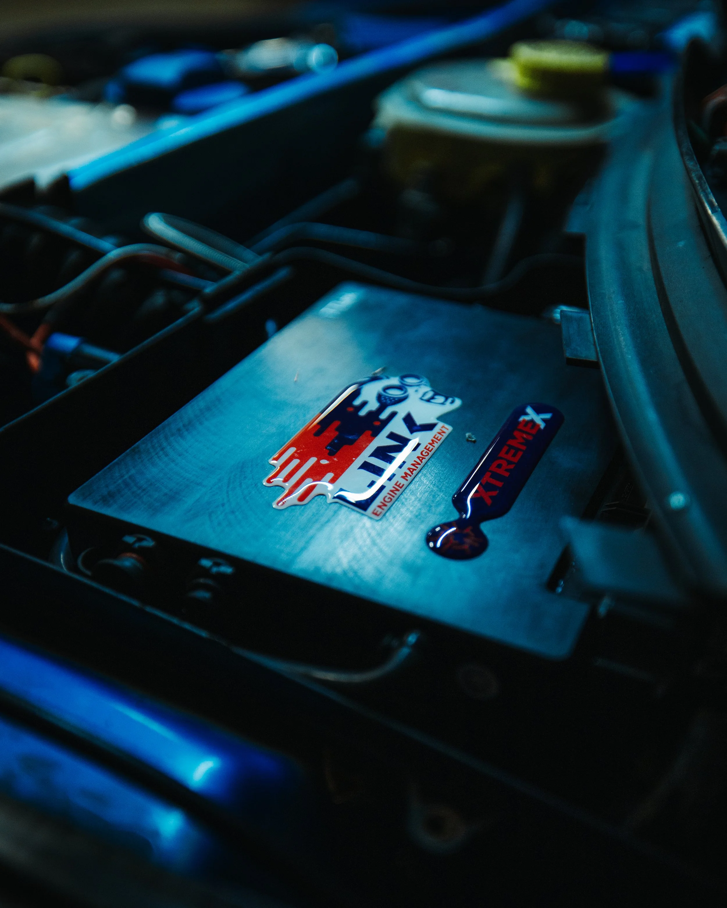 Close-up of a car engine showcasing stickers from GTX engine management and XtreME-X on the engine cover.