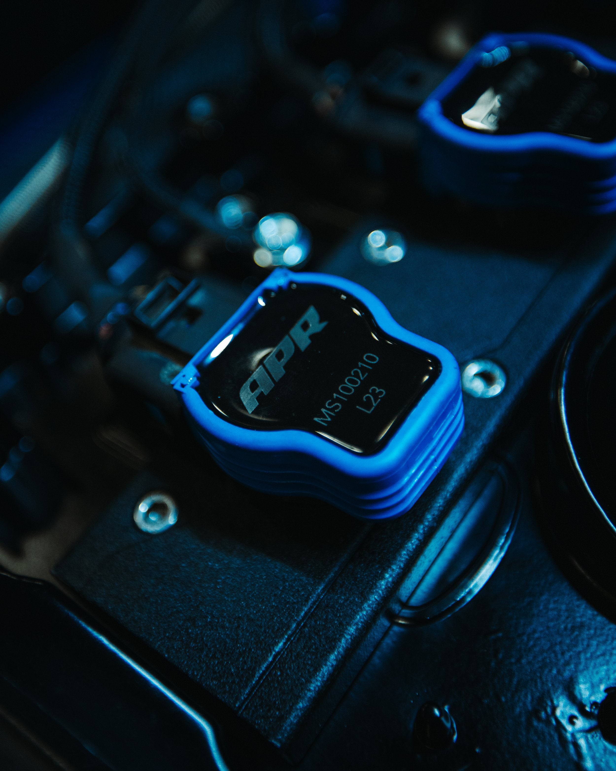 A close-up of a blue and black APR engine control unit on a black surface with other electronic components.