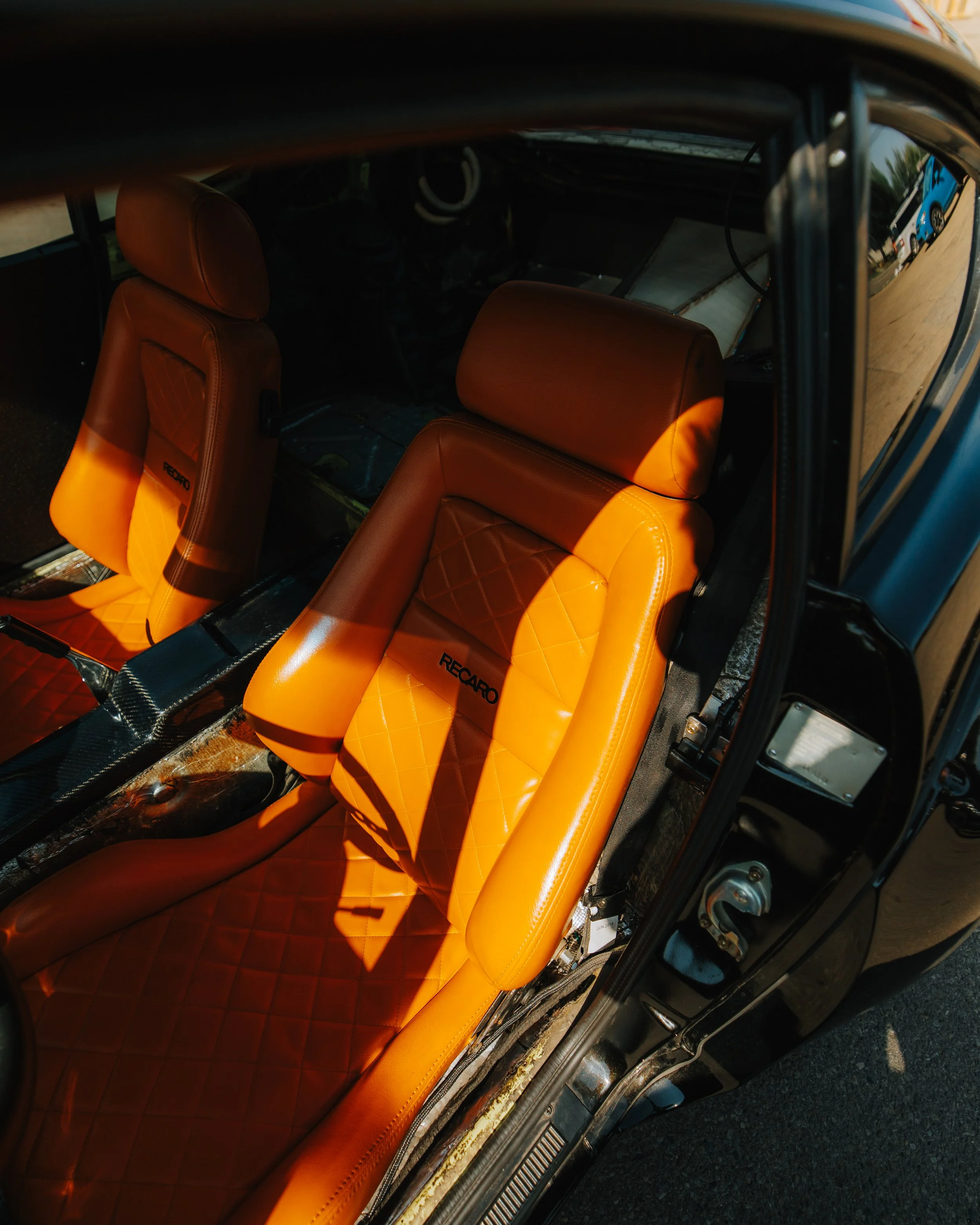 Close-up of orange Recaro racing seats inside a car with parts of the dashboard and side door visible.
