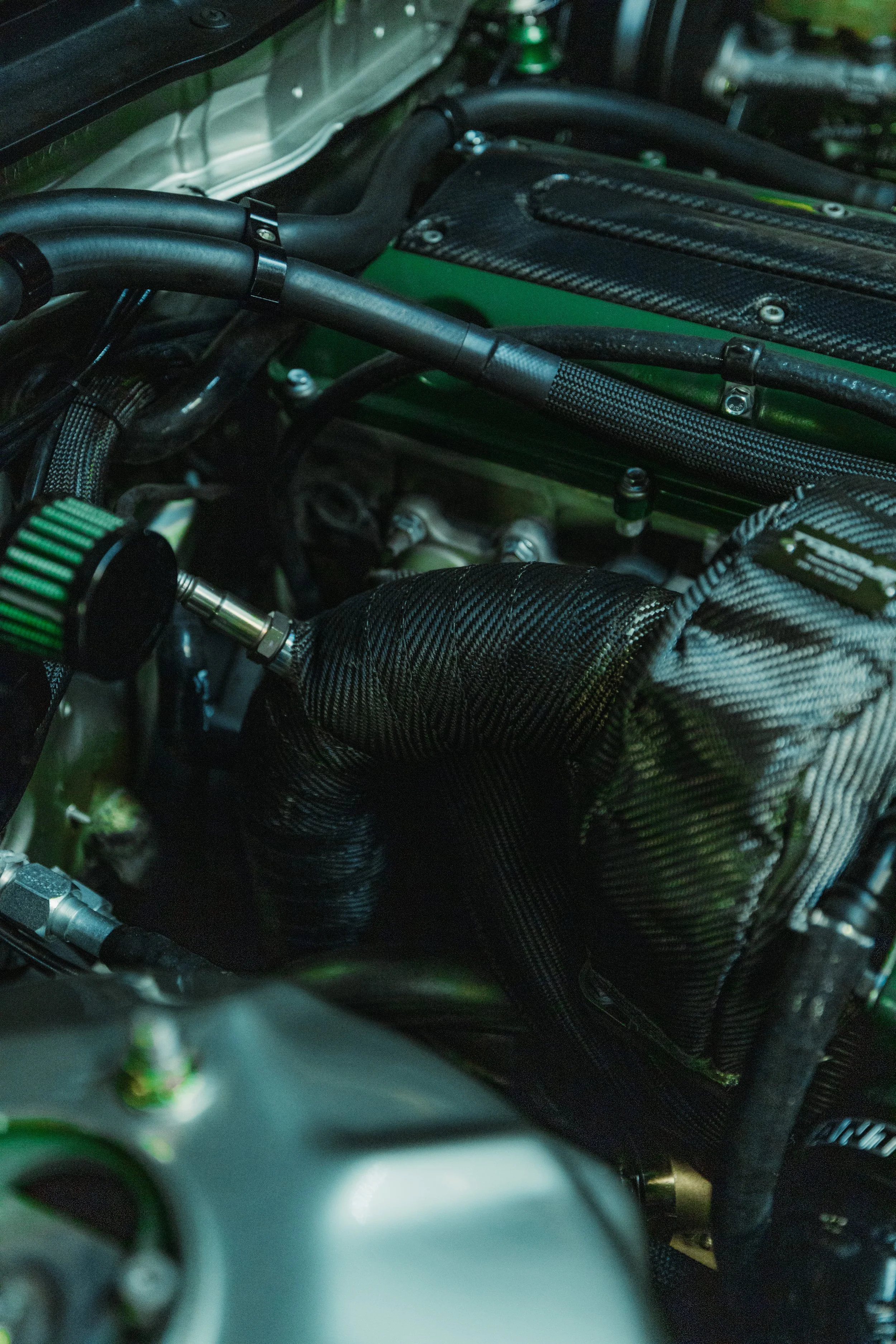 Close-up of a car engine with black hoses, a green filter, and various metallic components.