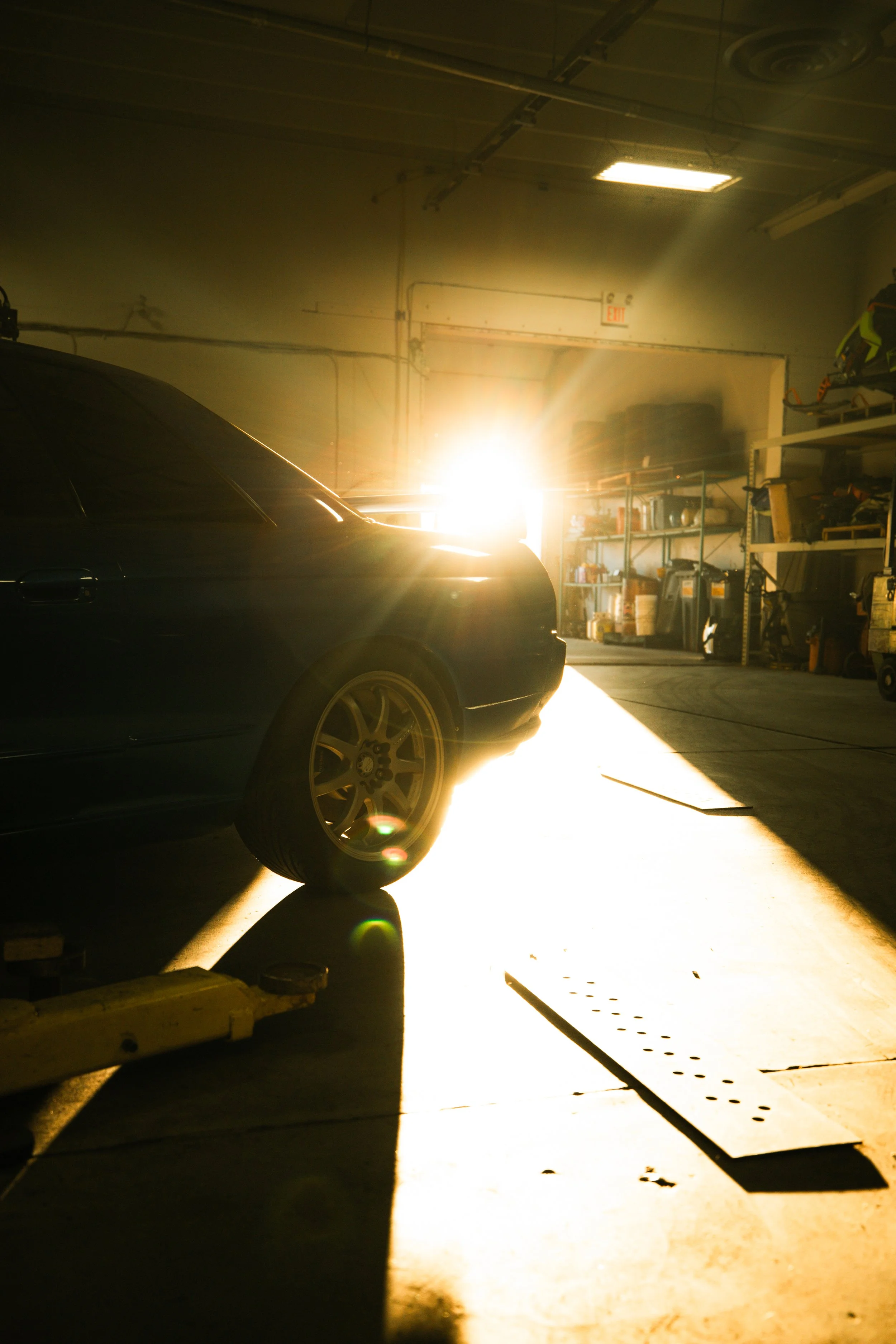 Side view of a car inside a garage with sunlight illuminating the floor and background.