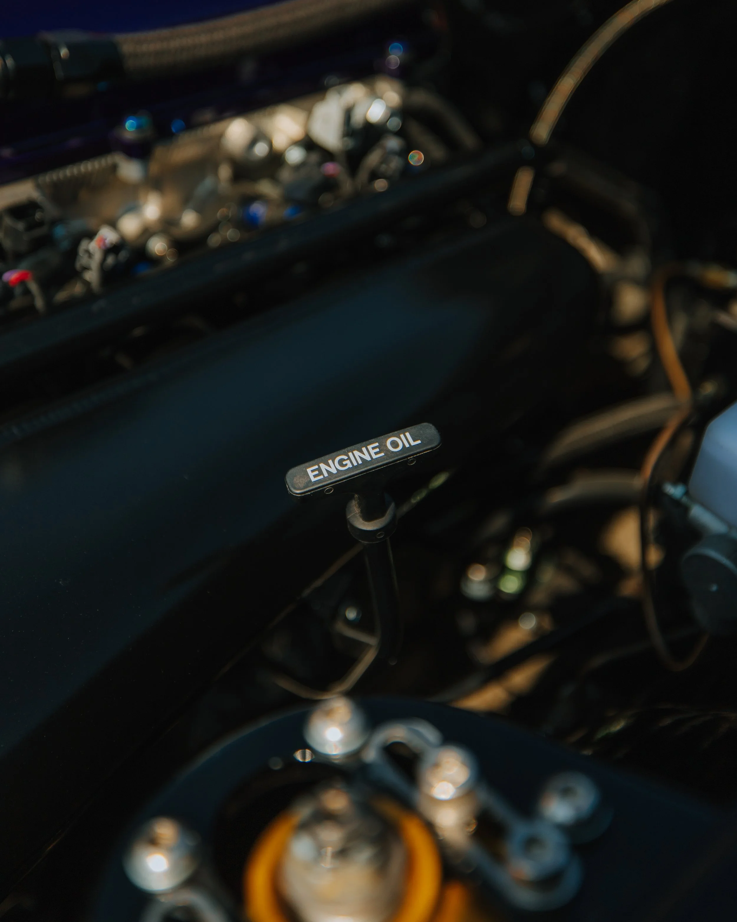 Close-up of a car engine showing a black engine oil cap labeled 'ENGINE OIL' and surrounding engine components and wiring.