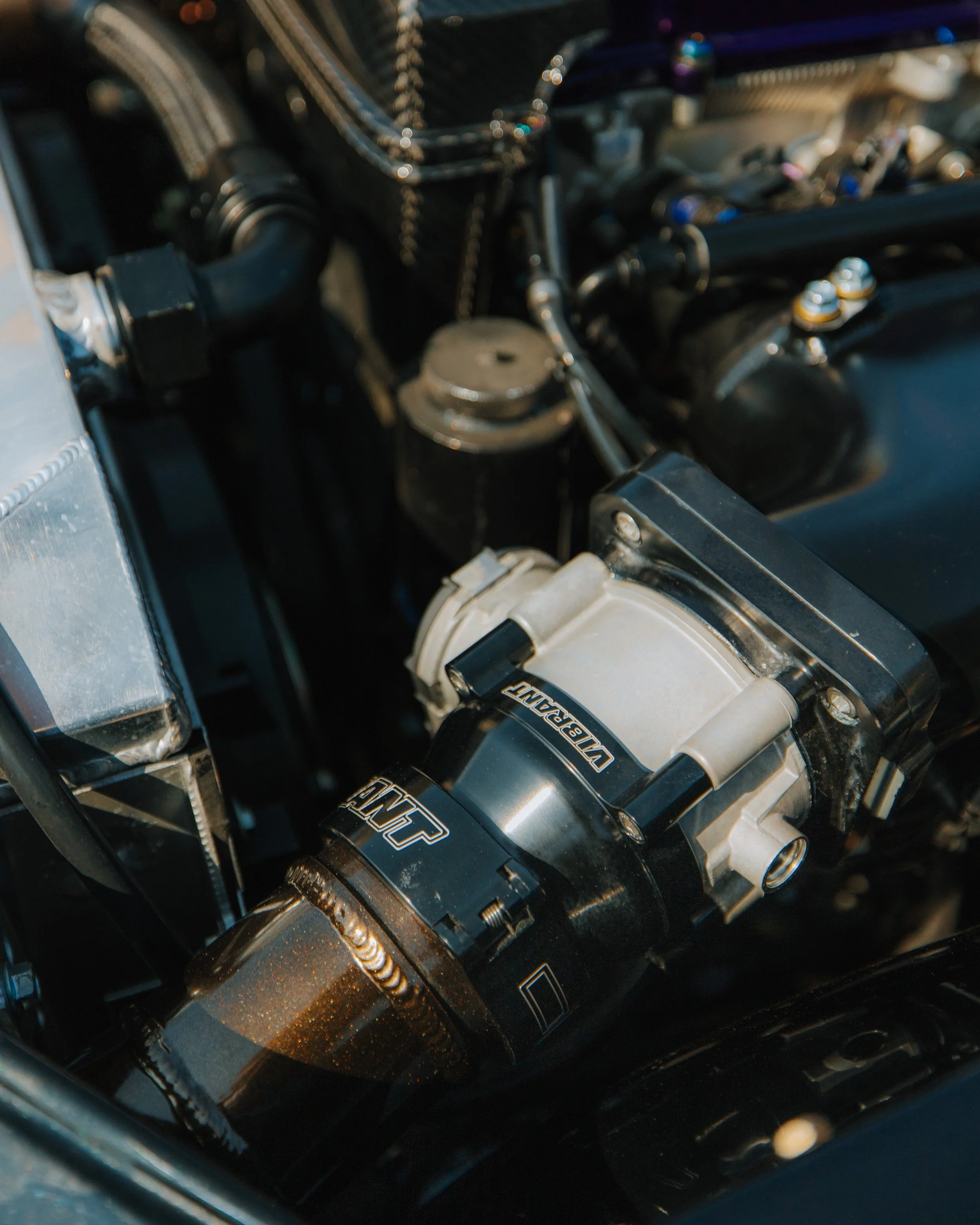 Close-up of a car engine showing a prominent black and silver supercharger with the brand name "VORTEX" and a metallic component around it.