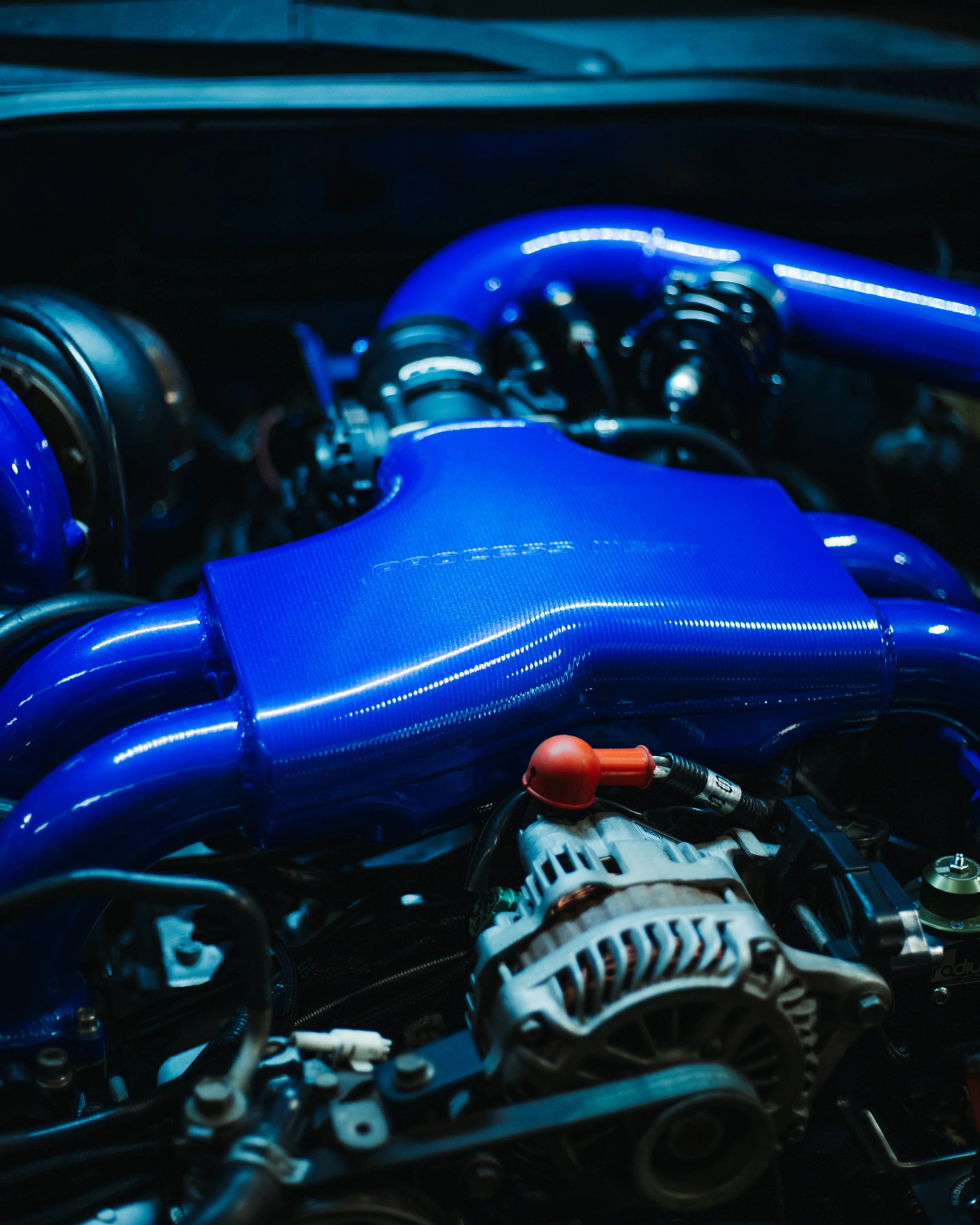 Close-up of a car engine with blue components, including an intake manifold, with various wires and parts visible.