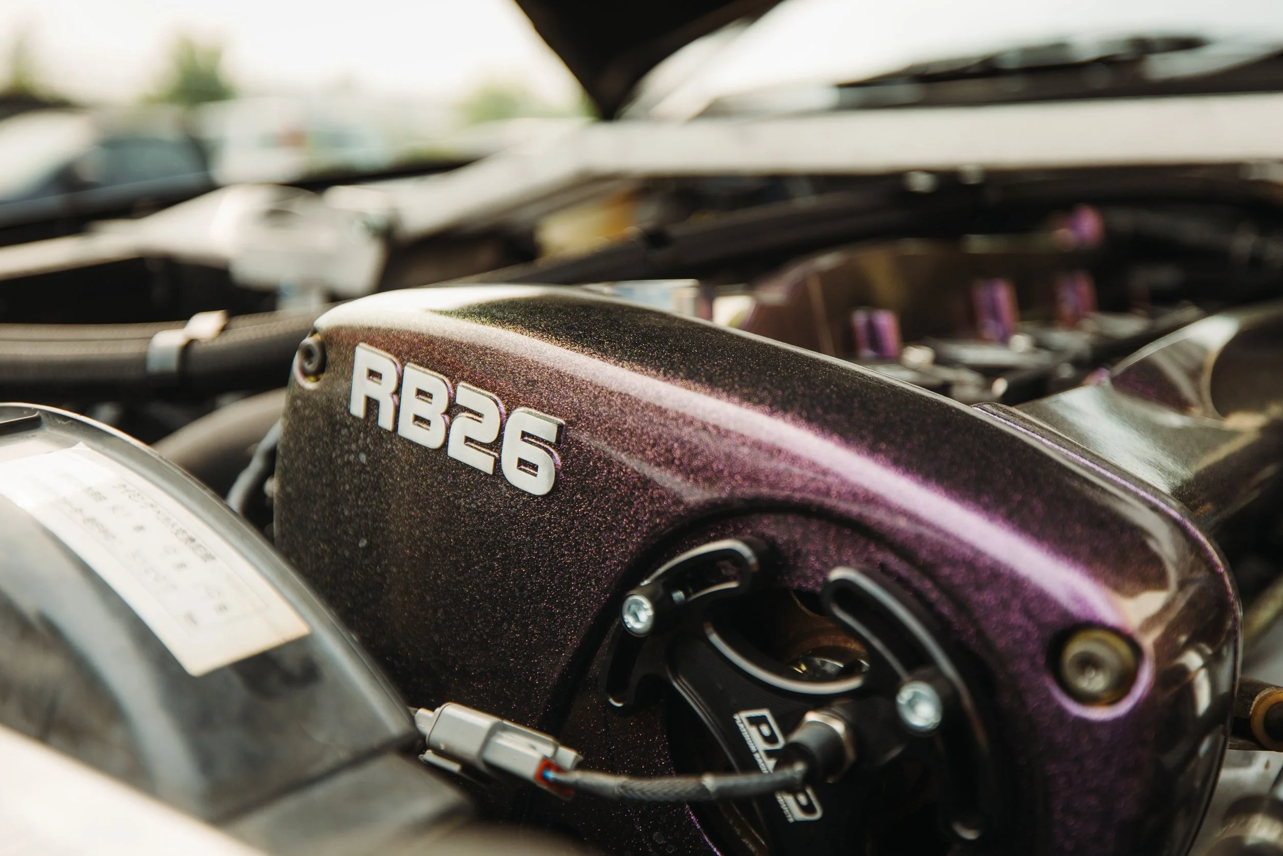 Close-up of a metallic purple engine component with the label 'RB26' on it, part of a car engine.