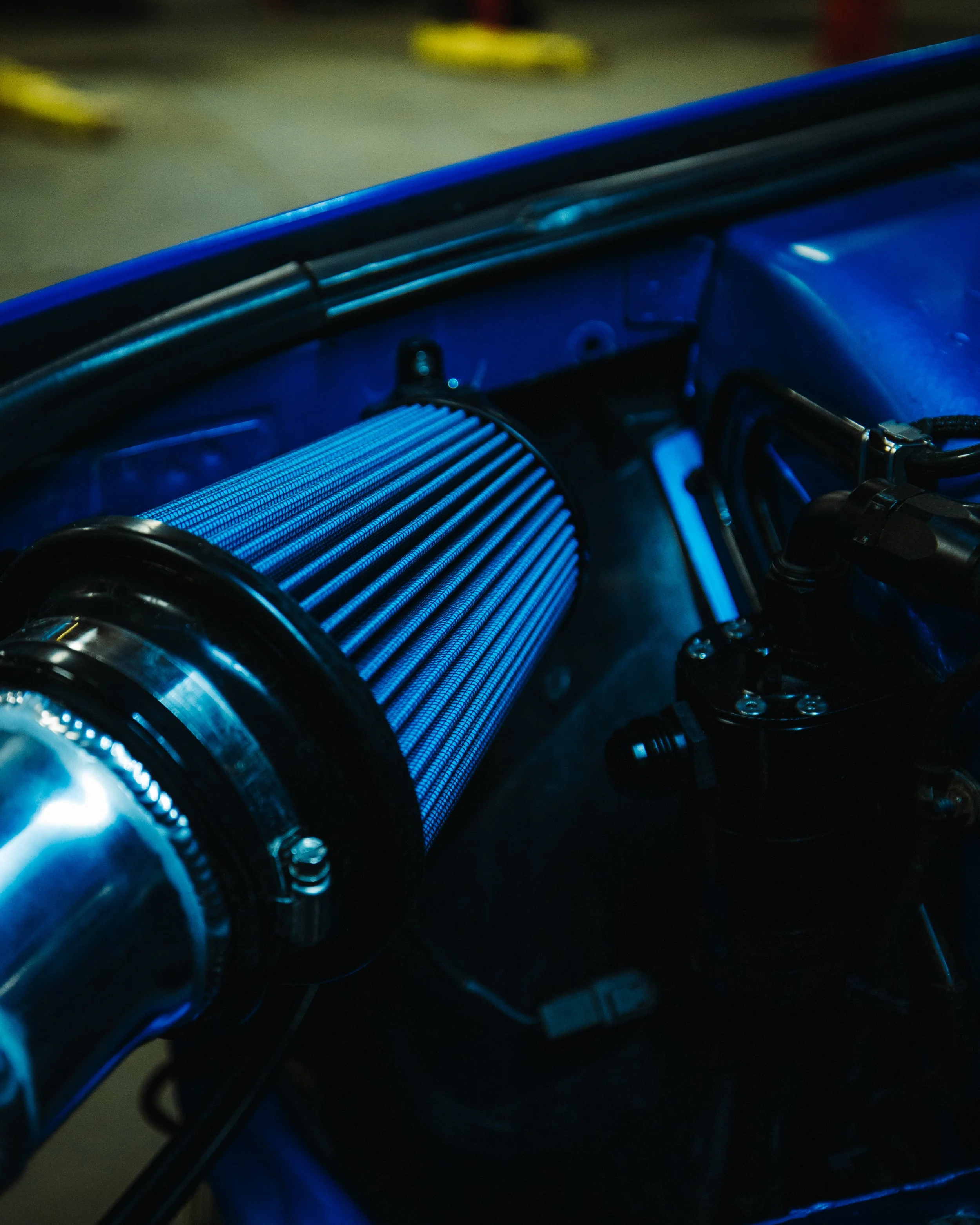 Close-up view of a car's aftermarket cold air intake system, featuring a conical air filter with a blue hue, mounted inside the engine bay.