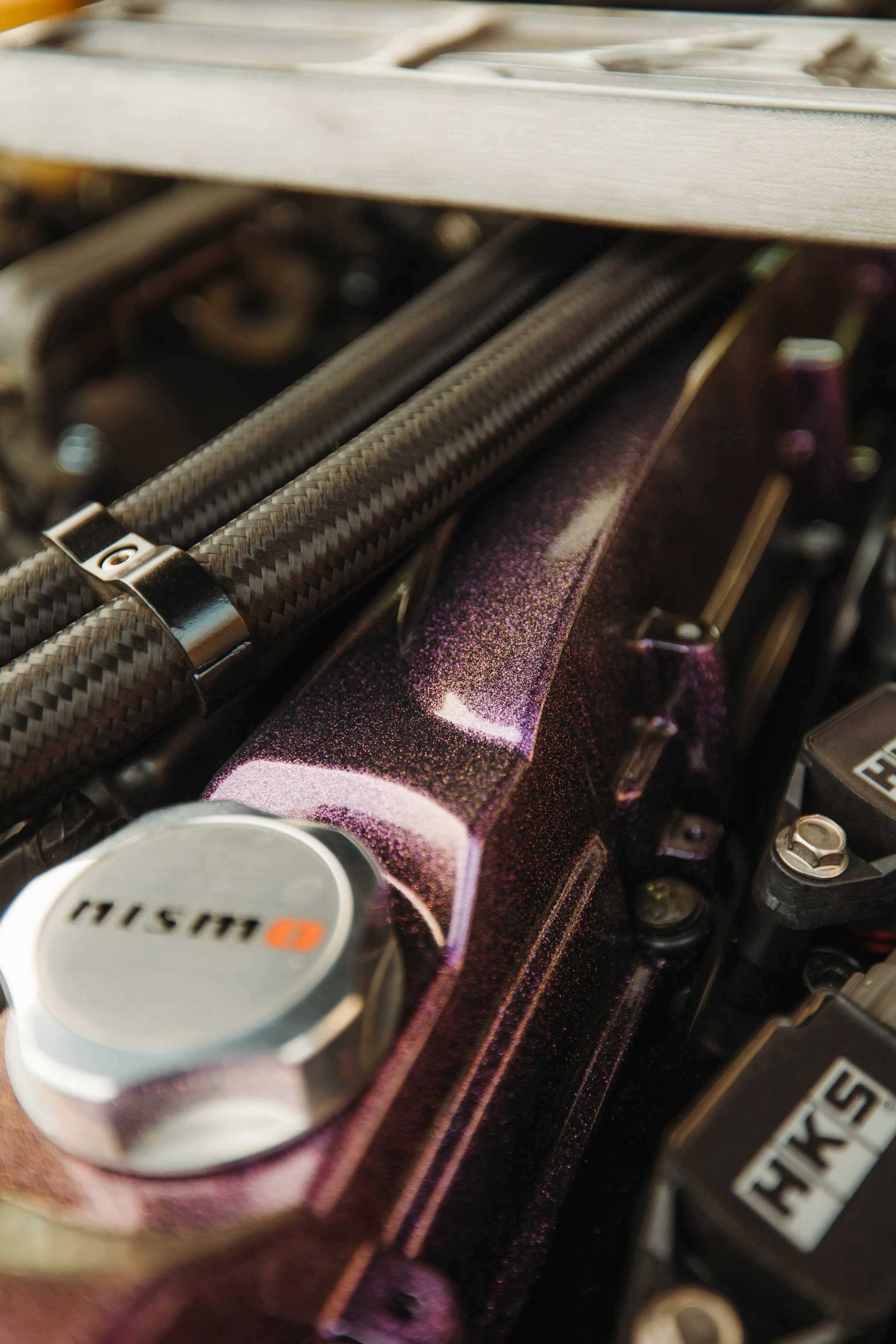 Close-up of a car engine showing a metallic purple engine cover, a silver cap labeled "Huski," and carbon fiber tubes.