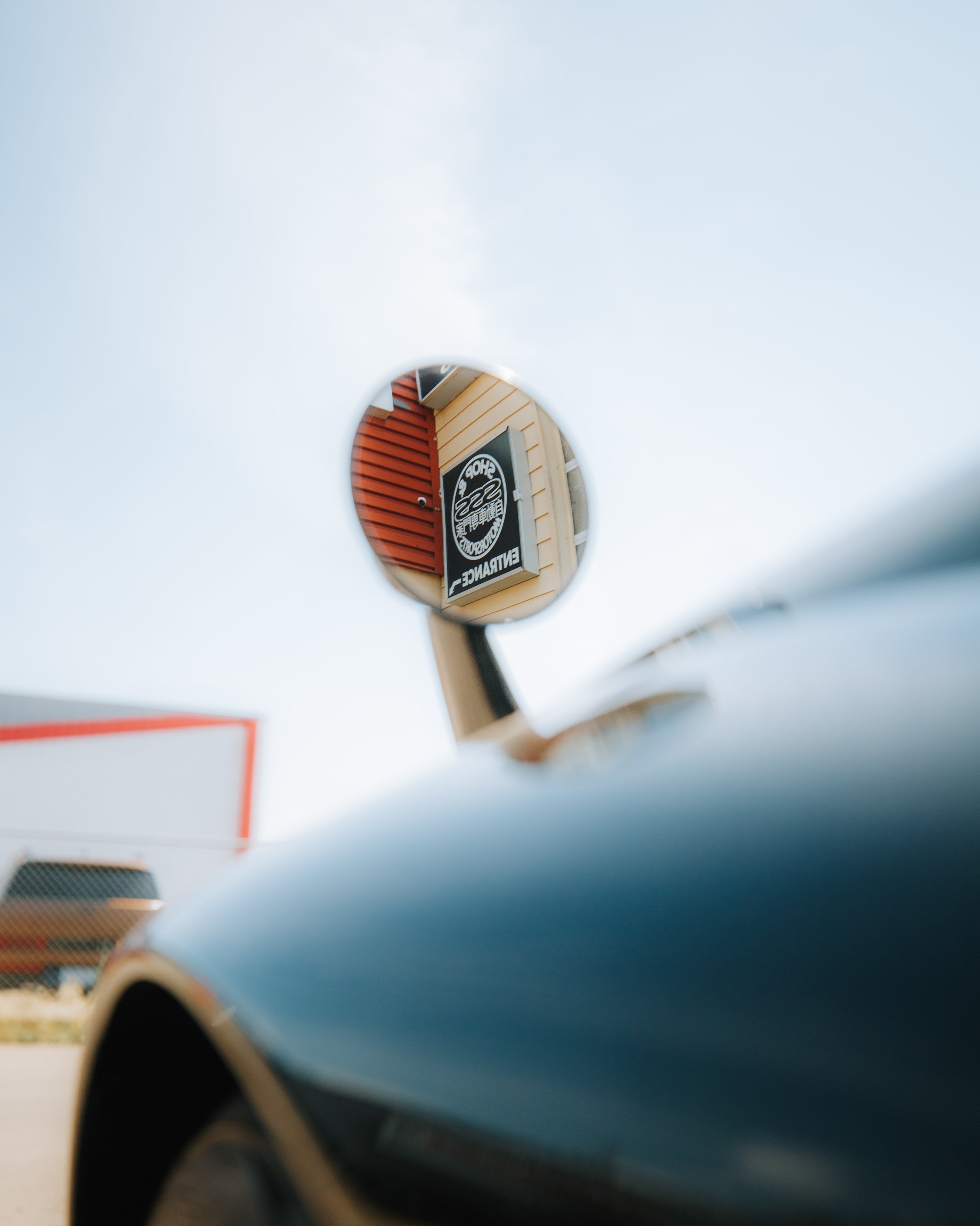 Close-up of a side mirror reflecting a sign and building exterior with colorful siding, in a parking lot.