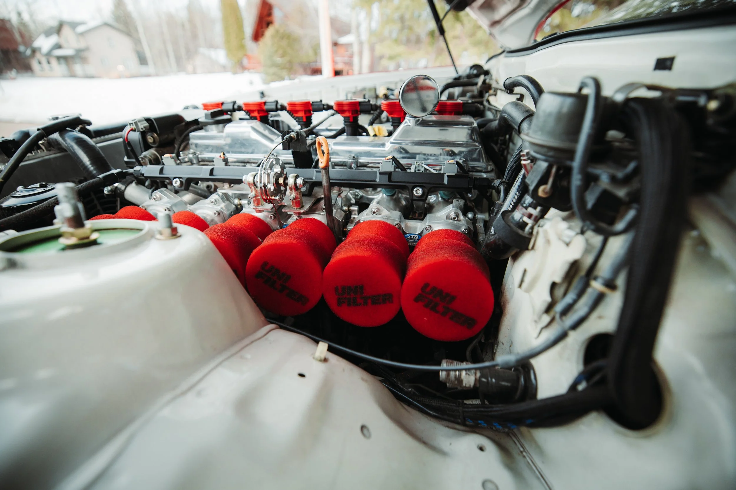Close-up of a race car engine with red air filters labeled UNi FILTER, silver components, and various hoses and wires.