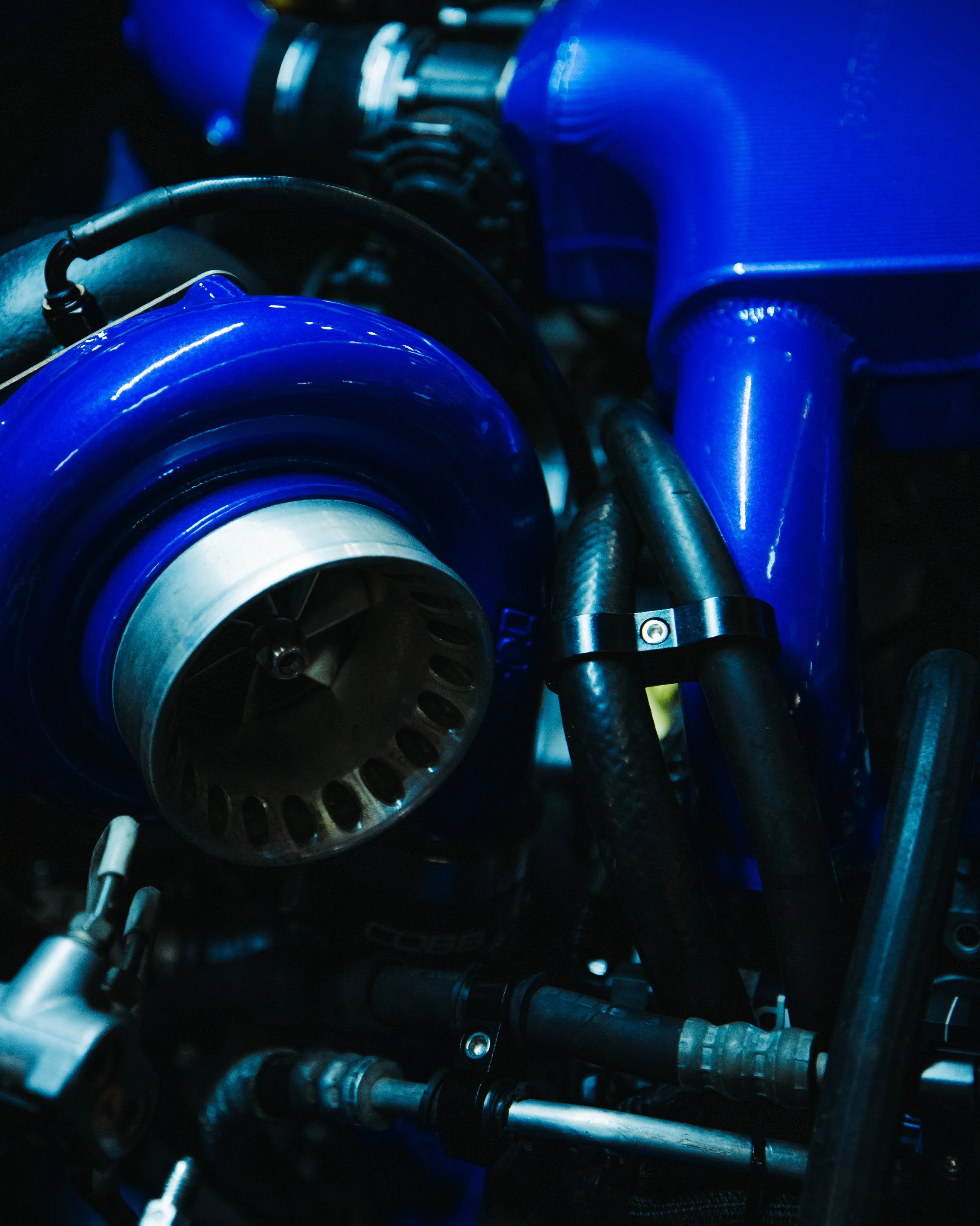 Close-up of a blue turbocharger among black pipes and components in an engine.