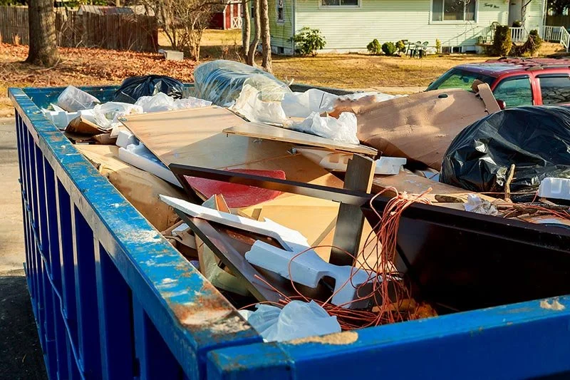 Overflowing blue dumpster filled with construction debris, wood, plastic, and wires.