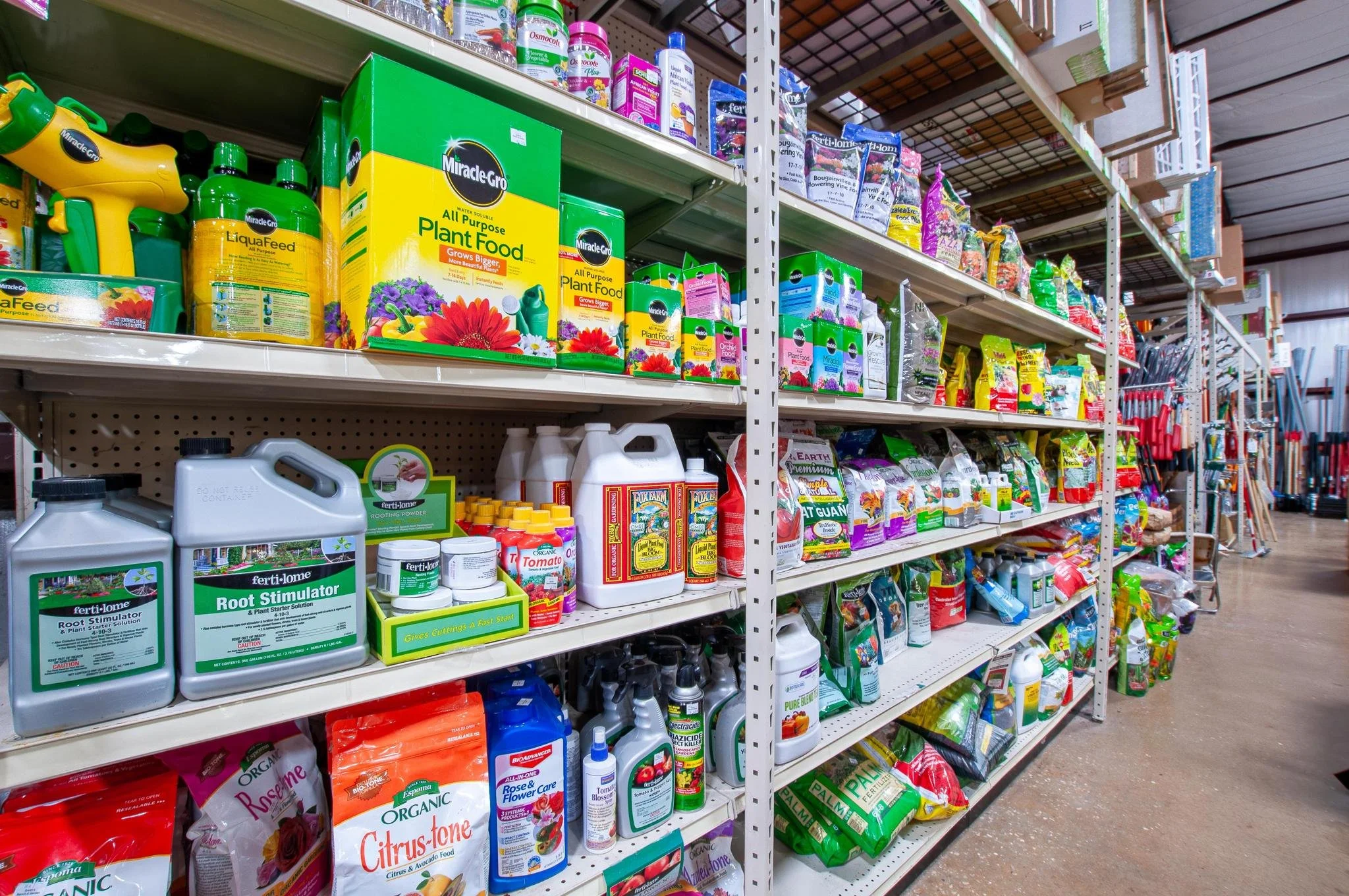 Aisle in a gardening store with shelves stocked with plant food, fertilizers, plant stimulants, and gardening tools.