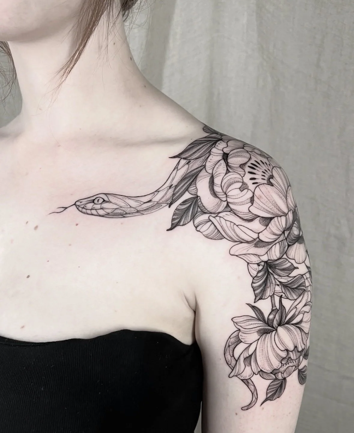 Un tatuaje en color negro en el hombro y brazo de un símbolo de serpiente entre flores y hojas.