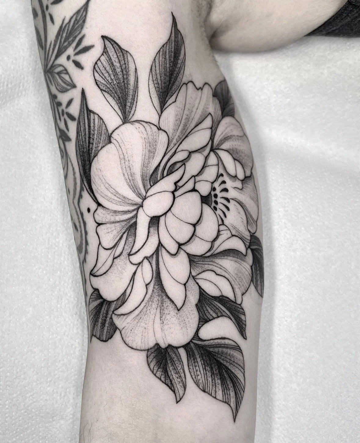 Tatuaje en blanco y negro de flores grandes y hojas en el brazo de una persona.