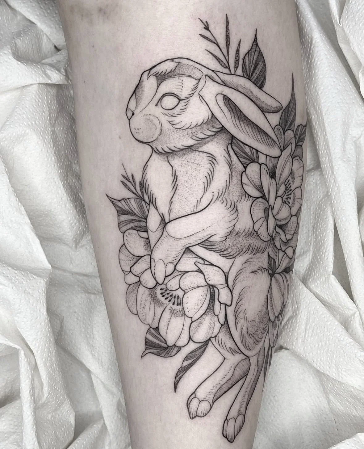Tatuaje en blanco y negro de un conejo con flores y hojas.