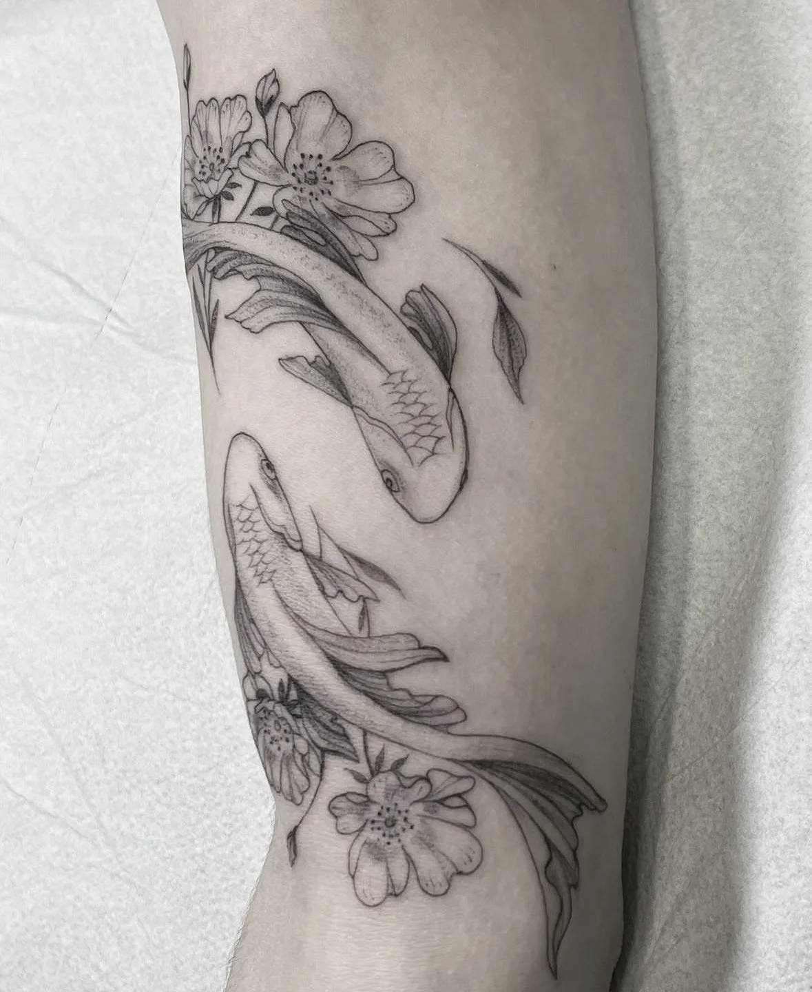 Tatuaje en el brazo con dos peces y flores.