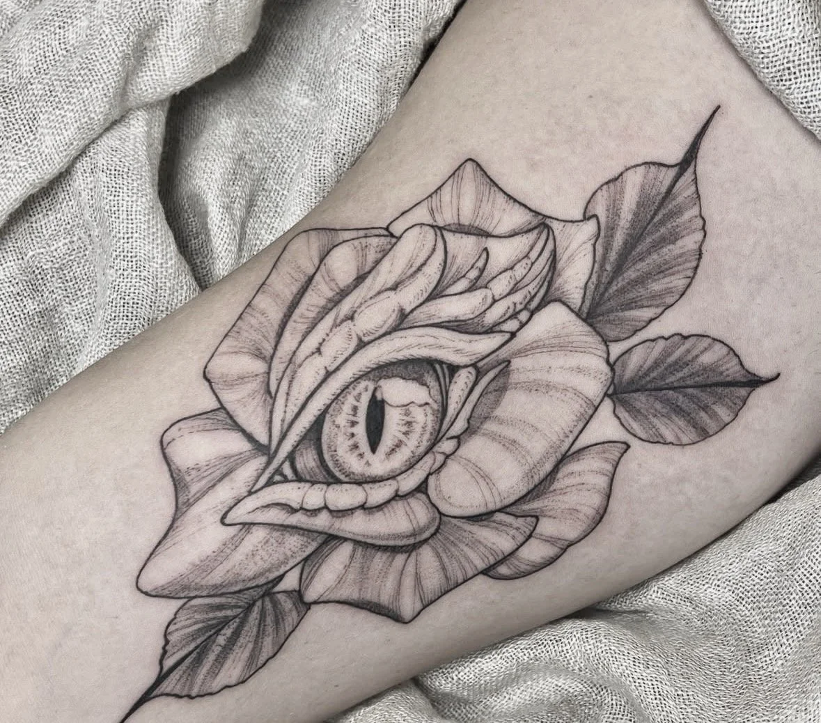 Tatuaje de una rosa con un ojo en el centro, en línea negra, en la piel.