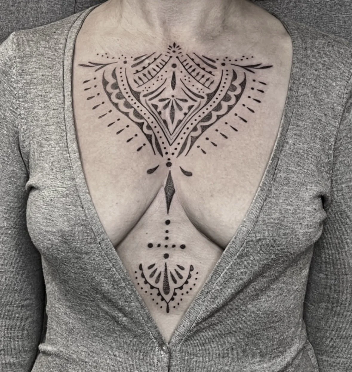 Tatuaje negro en forma de diseño geométrico en el pecho de una persona con ropa gris.