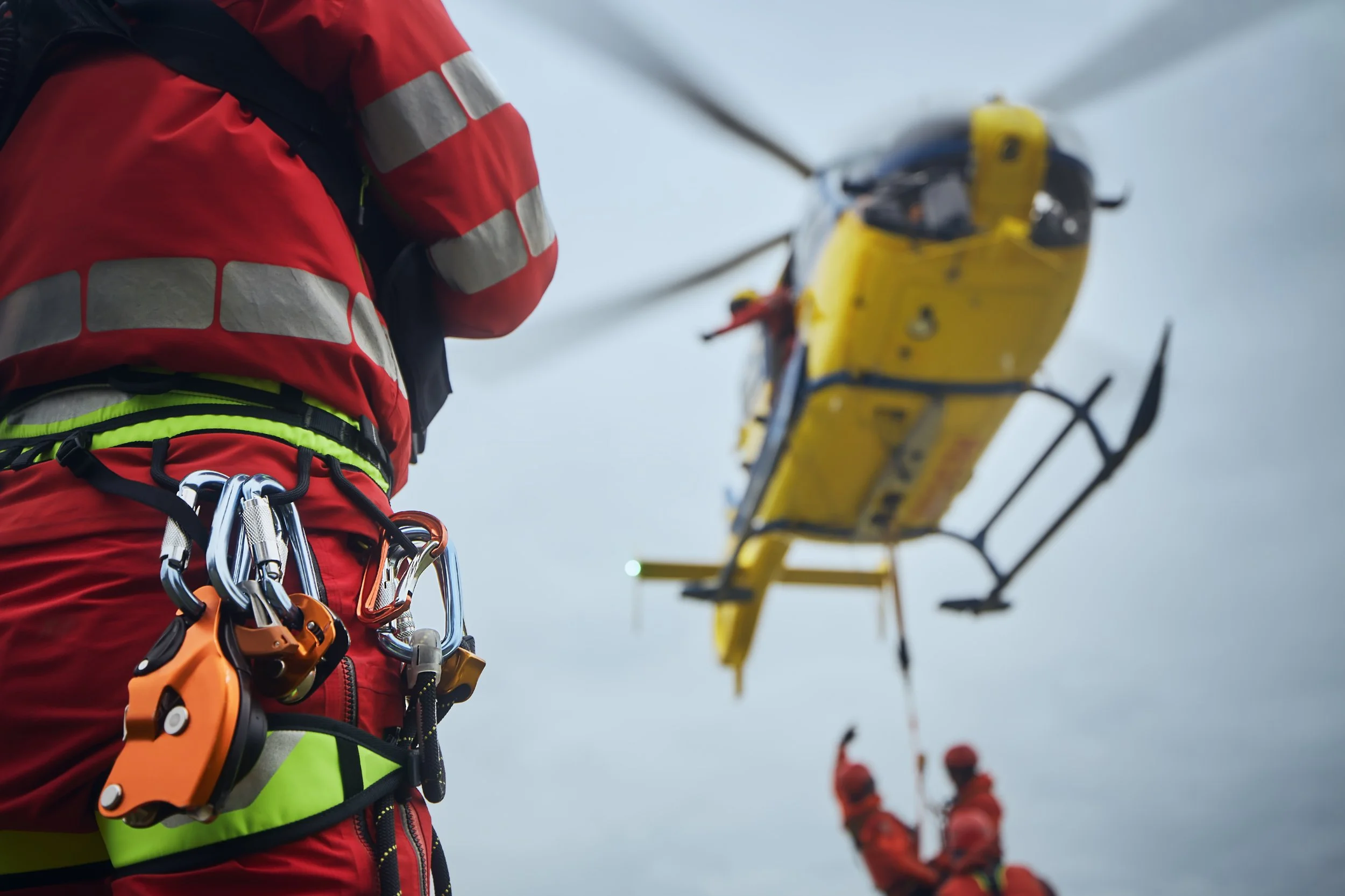 Rettungskräfte in roter Jacke mit Seil und Ausrüstung bereiten einen Hubschrauber für eine Rettungsmission vor.