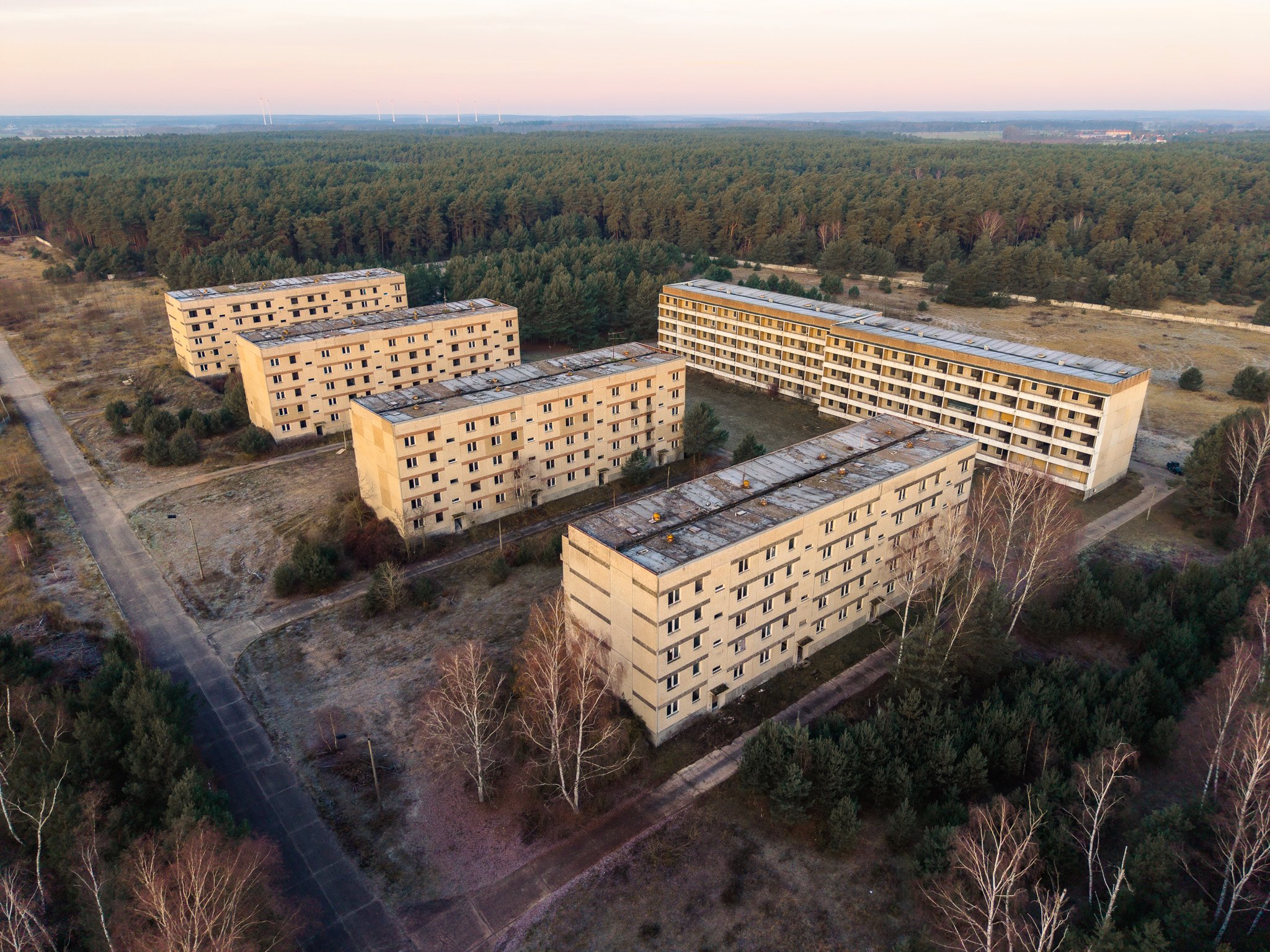 Luftaufnahme von fünf Apartmentgebäuden in einer ruhigen, bewaldeten Gegend bei Sonnenuntergang, mit einer Straße im Vordergrund.