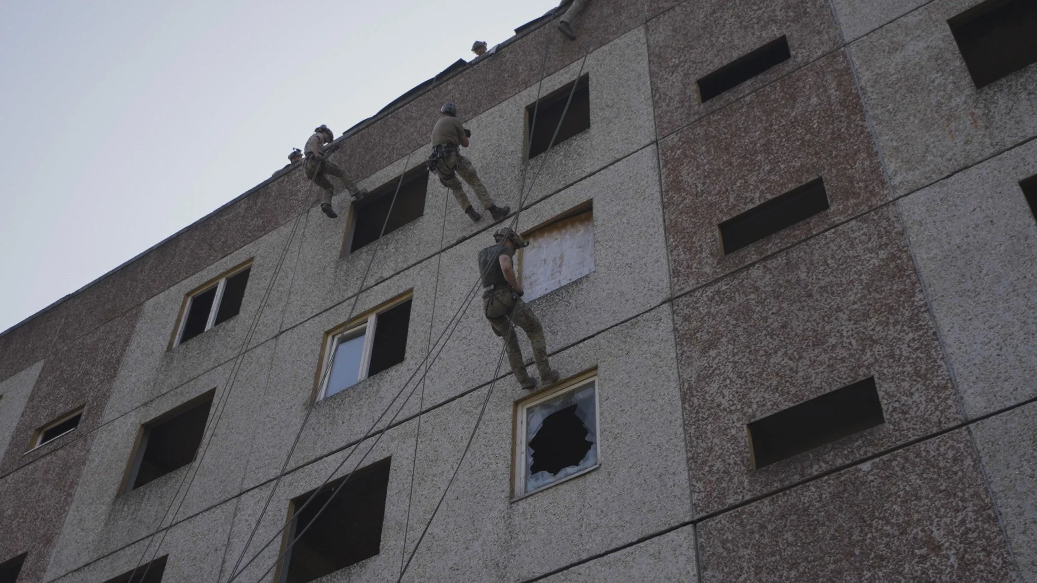 Soldaten reinigen die Fenster eines Hochhauses mit Seilen und Ausrüstung, einige Fenster sind zerbrochen.
