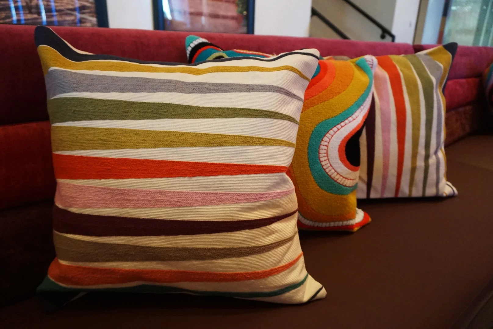 Three decorative pillows with colorful, striped, and patterned designs on a dark sofa.