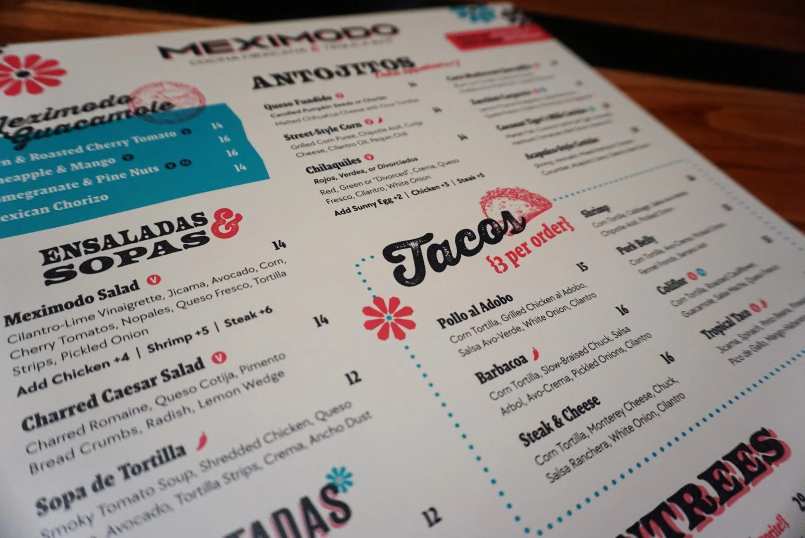 Close-up of a Mexican restaurant menu showing sections for salads, soups, and tacos, with items and prices.
