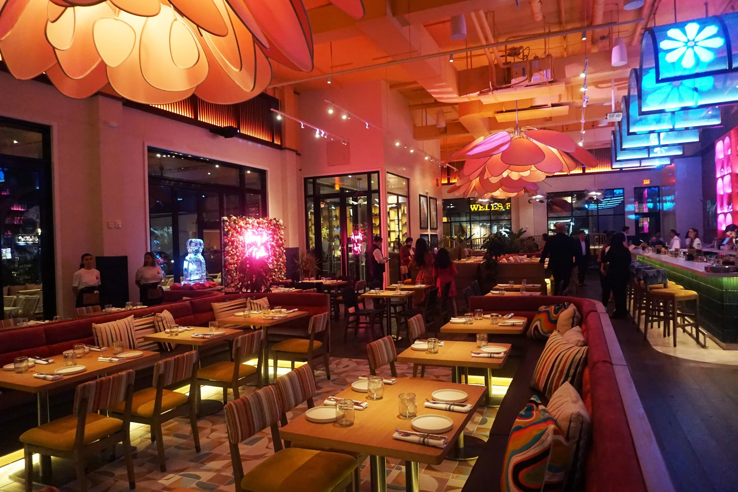 A vibrant, modern restaurant interior with colorful lighting, large floral-shaped ceiling fixtures, and neatly set tables for dining.