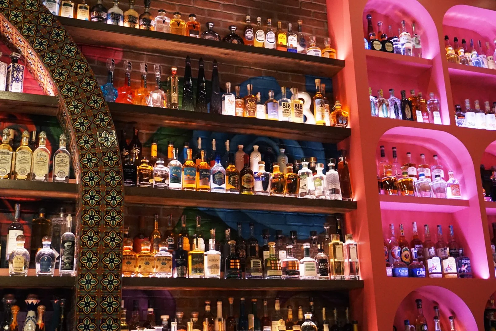 A bar with shelves filled with various bottles of alcohol, illuminated by colorful pink and purple lighting.