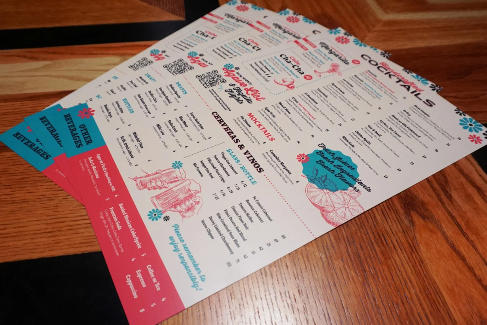 Colorful restaurant menu on a wooden table, featuring drinks, cocktails, and beverages, with decorative floral and citrus illustrations.