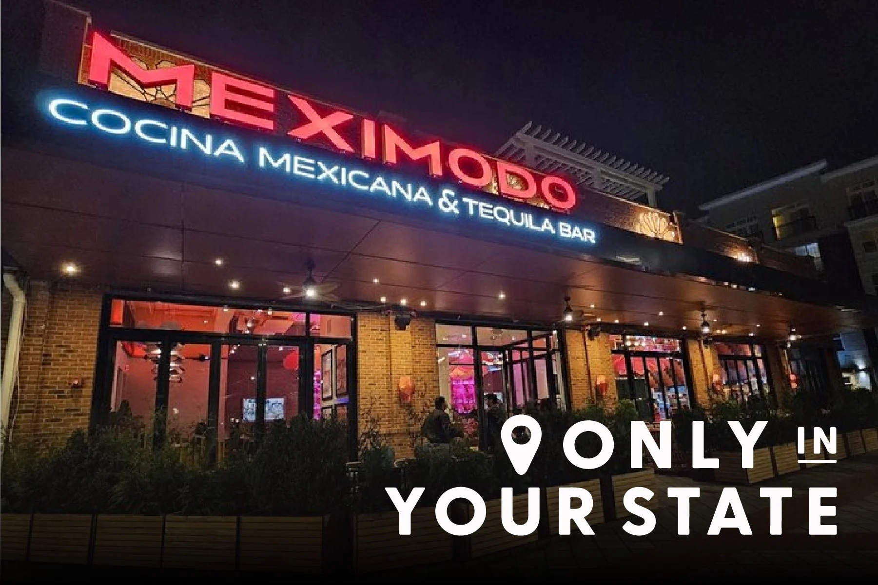 Night view of a Mexican restaurant with a large neon sign that reads 'TEXIMODO' and smaller sign below that says 'COCINA MEXICANA & TEQUILA BAR'. Many windows and a few people sitting outside.