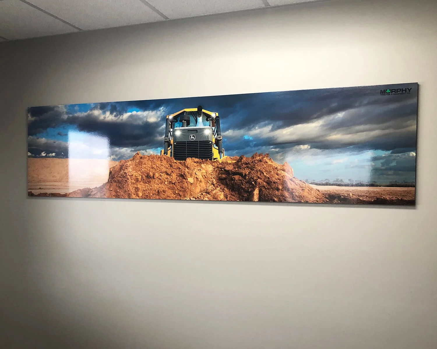 Panoramic photo of a construction site with a yellow and black bulldozer on a mound of dirt, against a cloudy sky landscape.