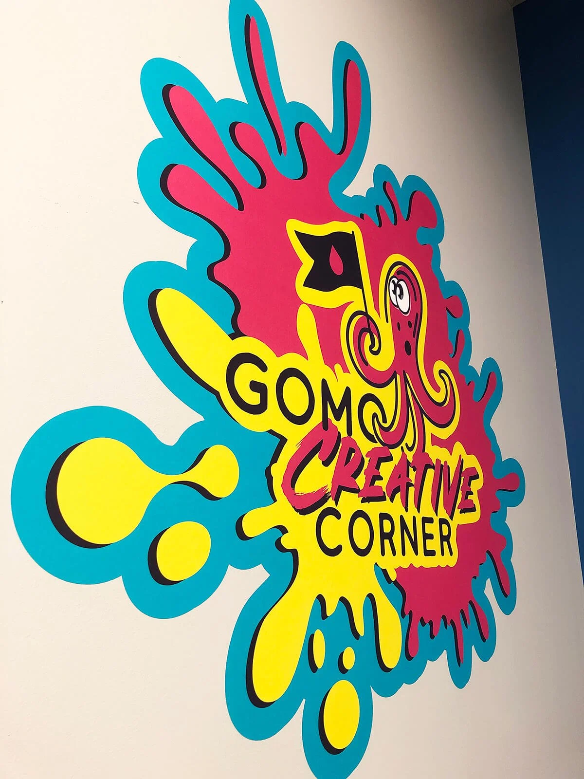 Colorful decorative wall art with a pink, yellow, and black octopus illustration, and the words 'GOMU CREATIVE CORNER' written in bold letters.