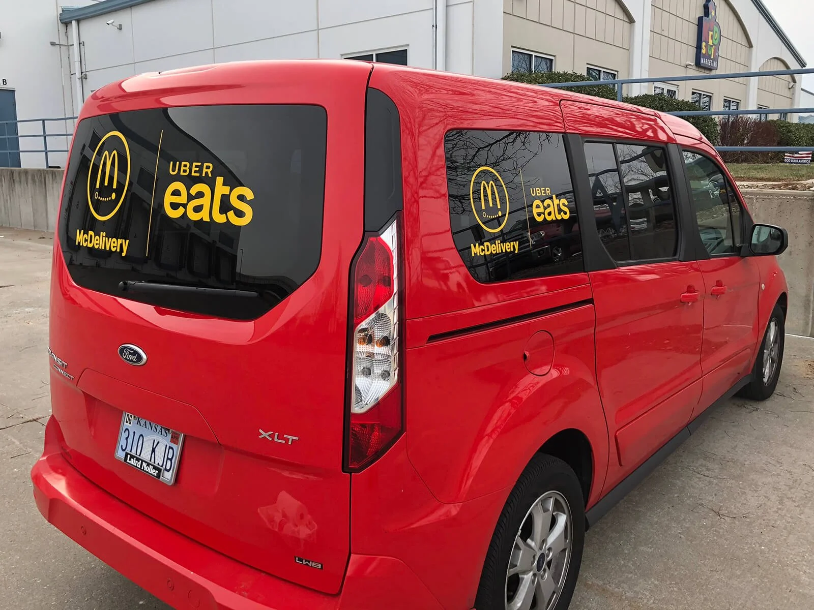 Red Ford Transit van parked outdoors with Uber Eats McDelivery stickers on the rear and side windows.