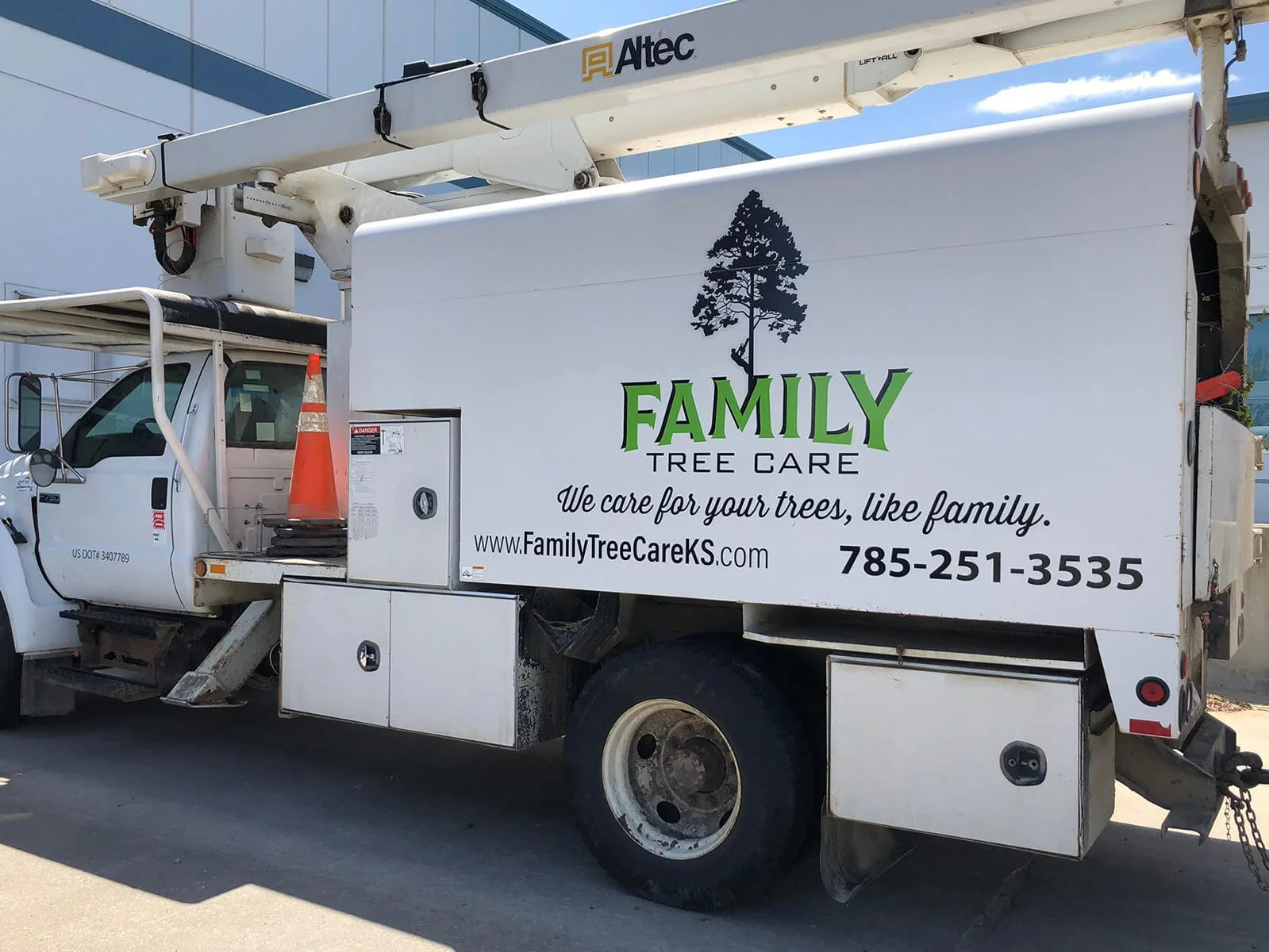 A utility truck with a sign for Family Tree Care, a tree care service, parked outside a building. The sign features a pine tree graphic and the text 'FAMILY TREE CARE,' 'We care for your trees, like family,' along with a website address and phone num